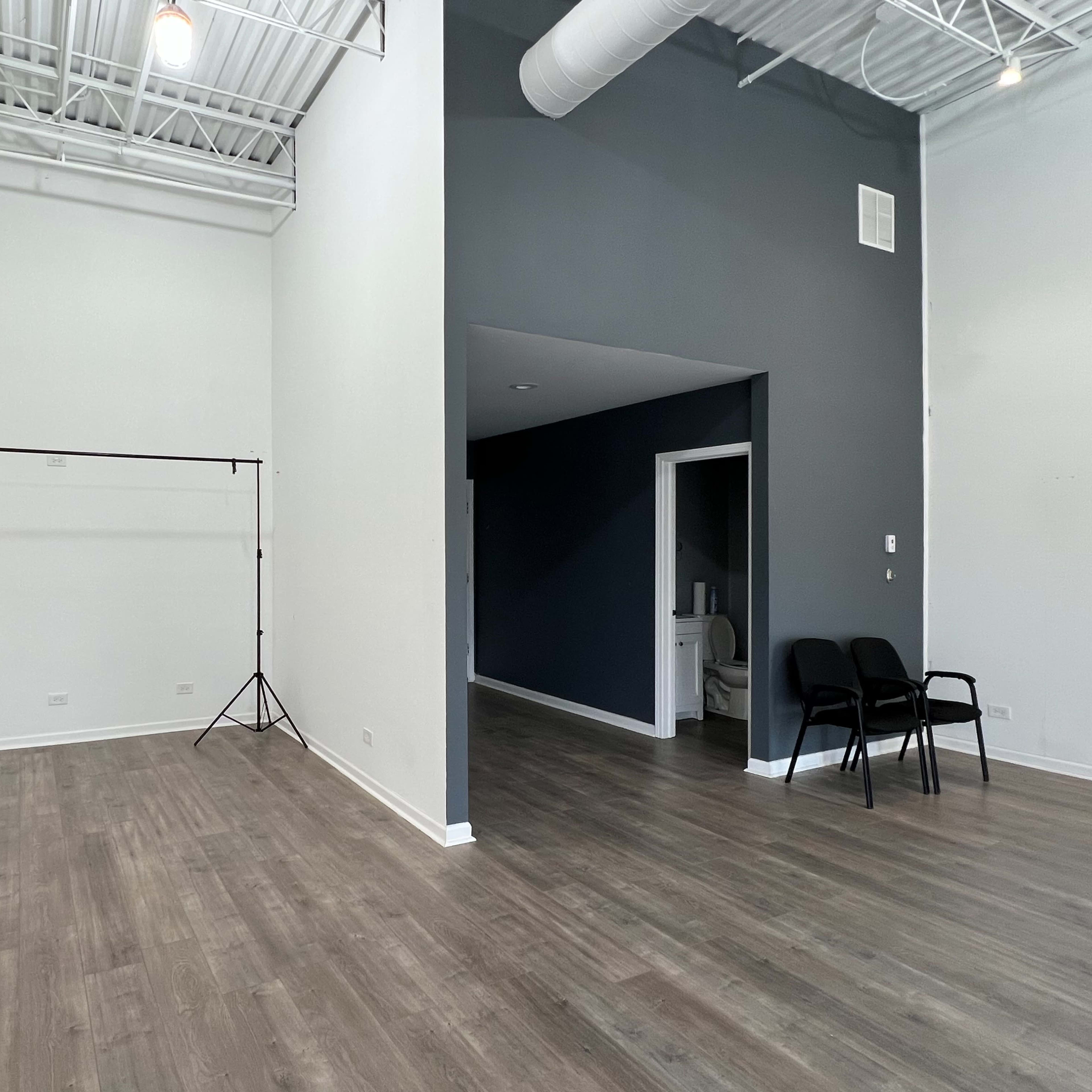 A spacious, minimalistic room with light wood flooring, a dark gray accent wall, and a simple backdrop setup in the corner.