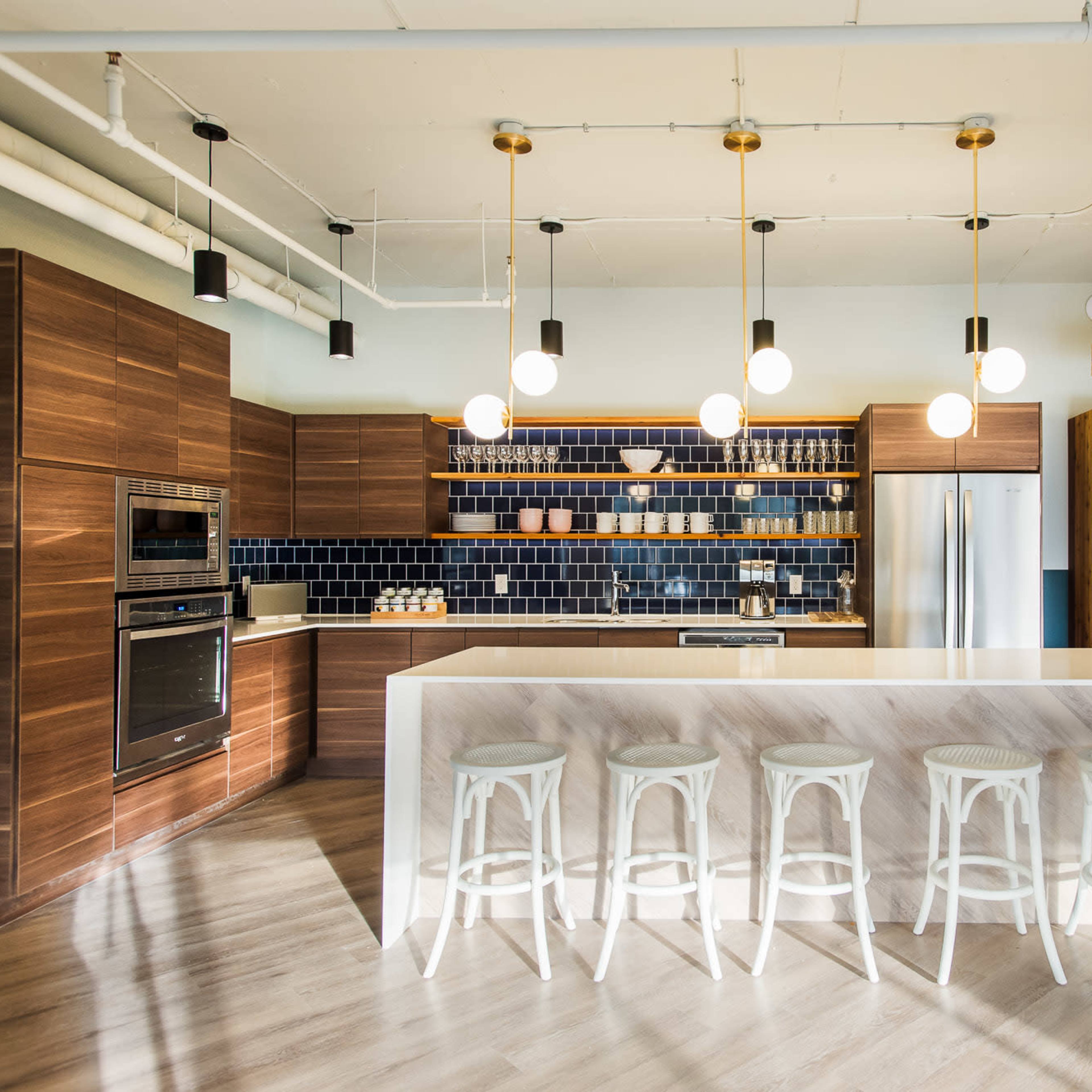 A modern kitchen with wooden cabinetry, a spacious island with white stools, and overhead pendant lights.