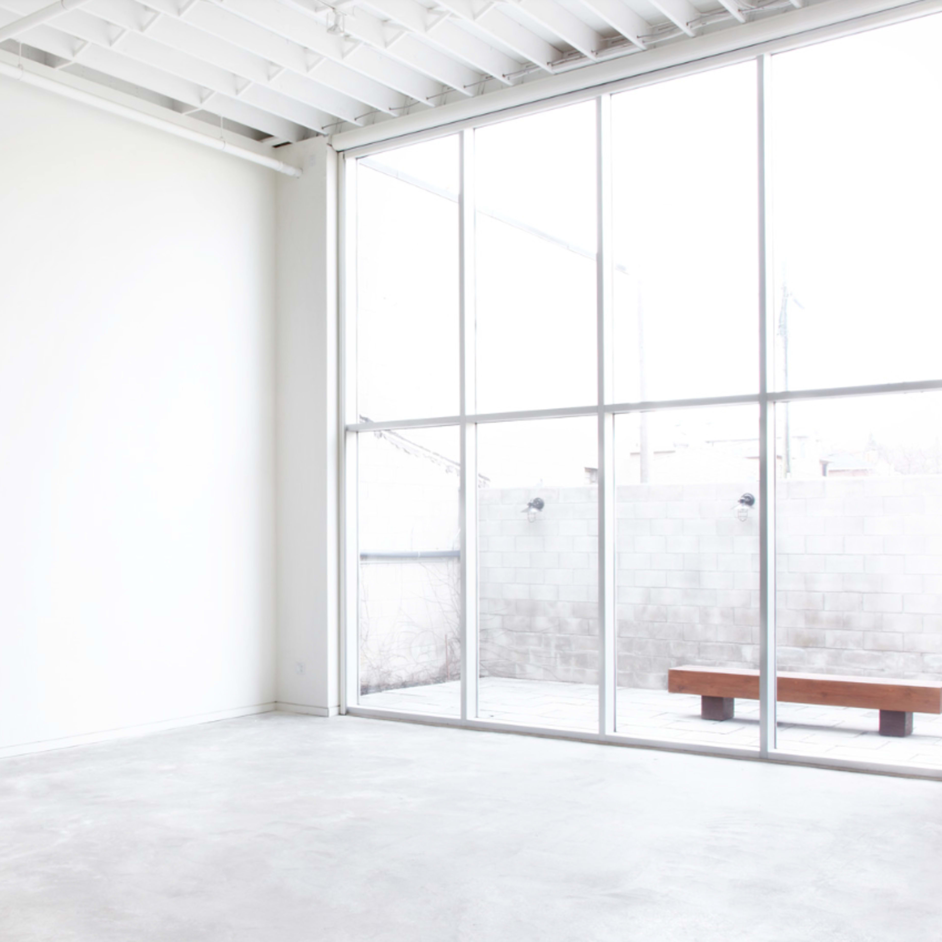 A spacious, bright room with a large window overlooking a small outdoor area and a minimalistic wooden bench.