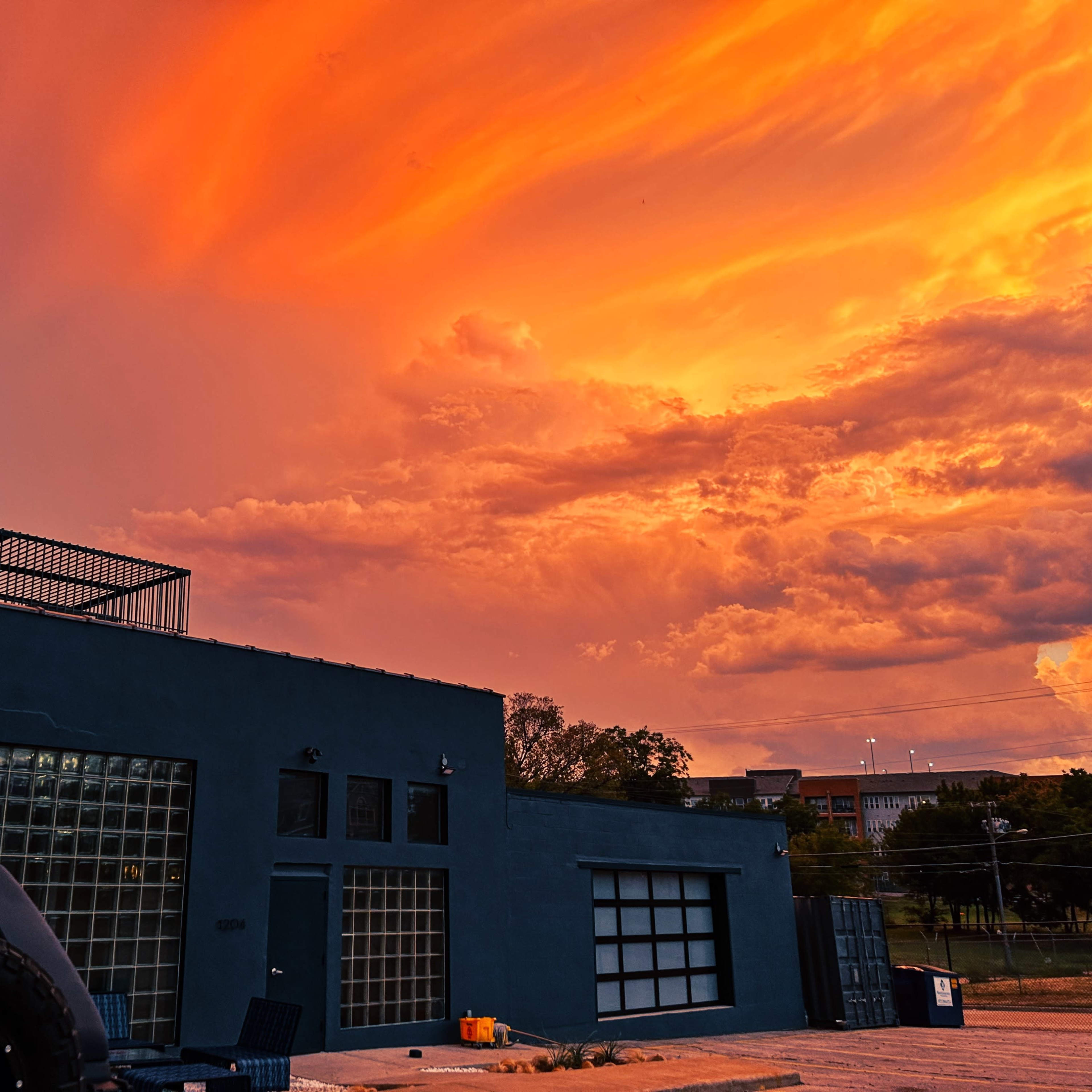 A dark blue building with large windows stands against a vibrant orange and purple sunset sky.