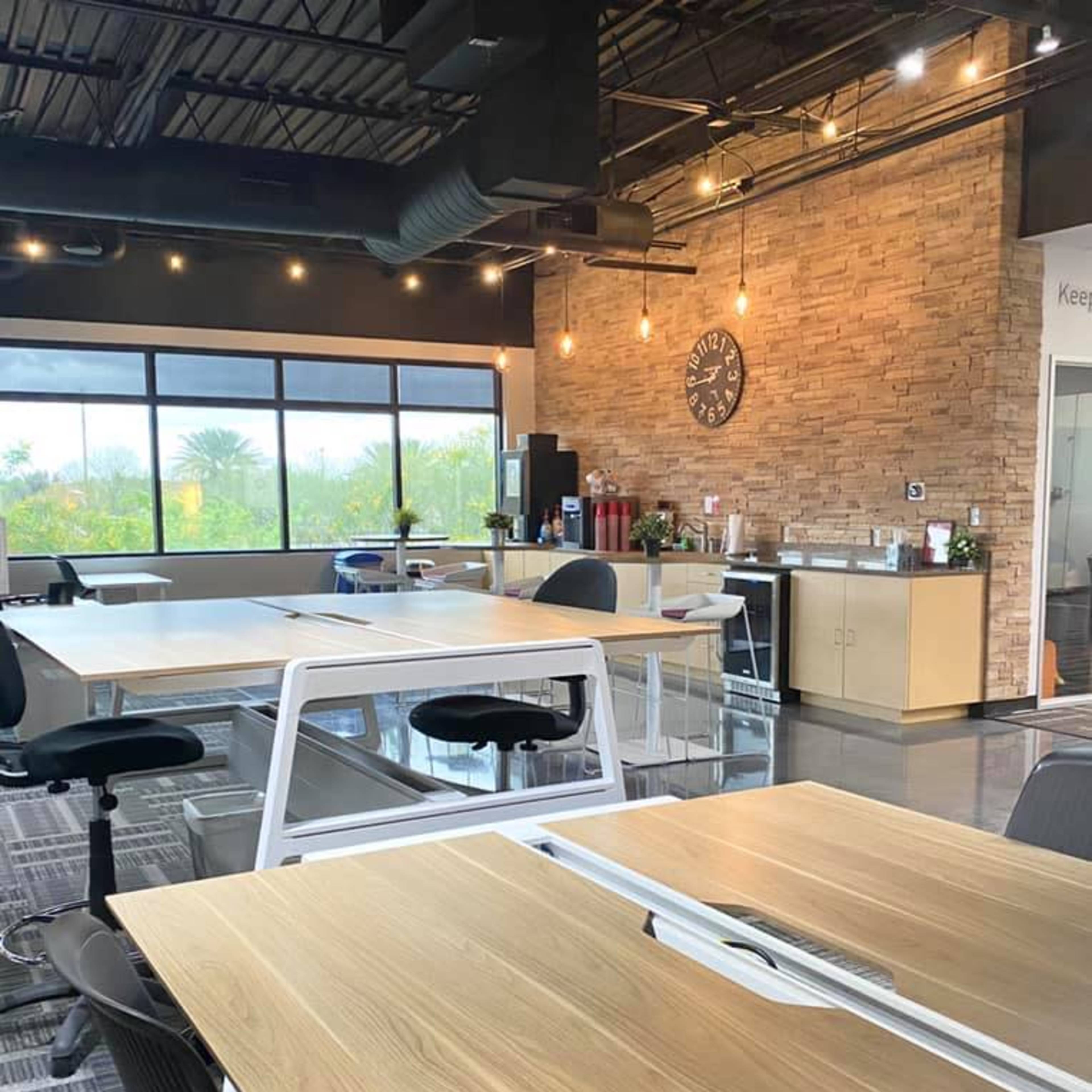 A modern office space with several wooden desks, black office chairs, and large windows letting in natural light.