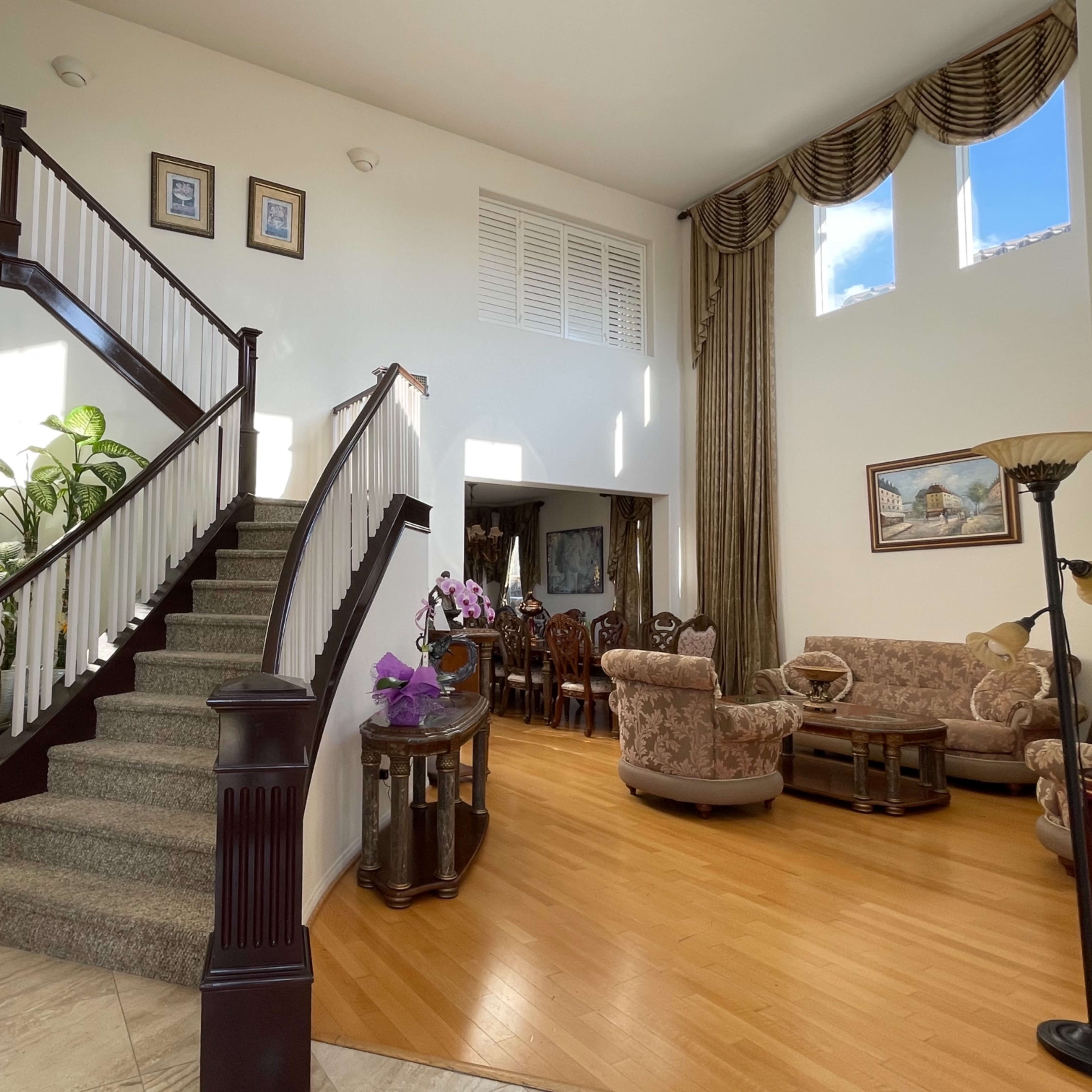 A spacious foyer with a staircase leading to an upper level, adjacent to a living area furnished with chairs and a large window.