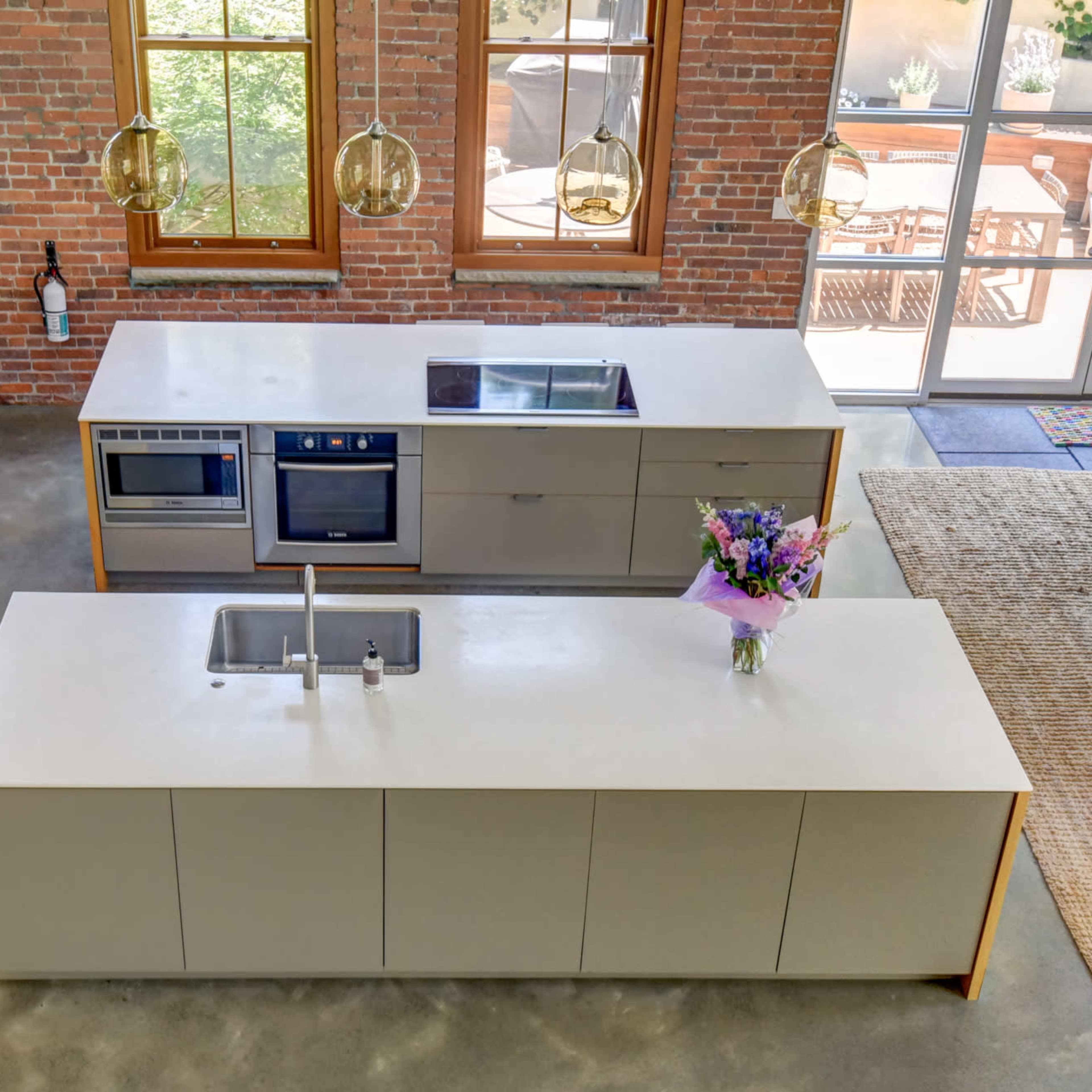 A modern kitchen featuring a central island with a sink, surrounded by sleek cabinetry and large windows allowing natural light to enter.