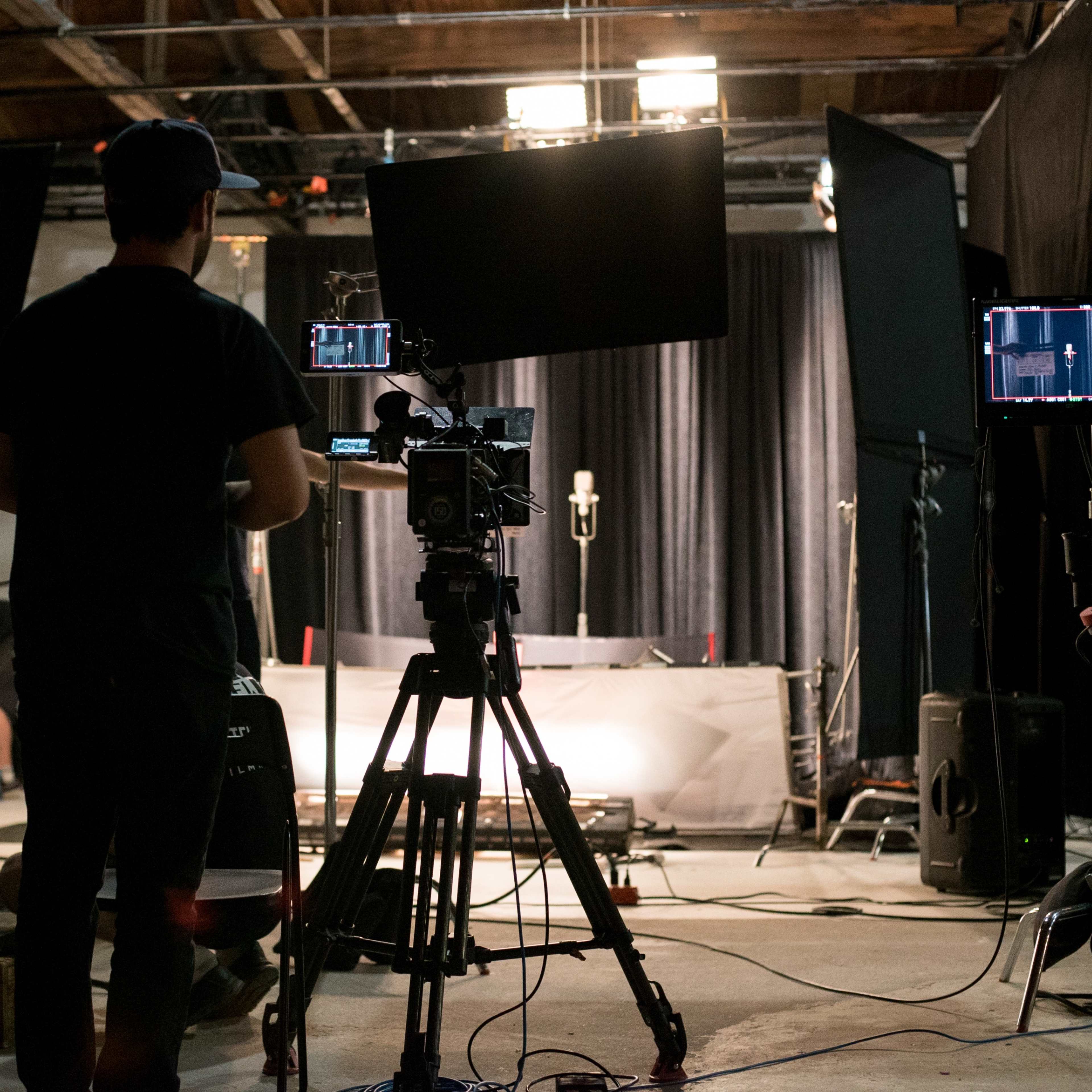 A film crew sets up equipment in a studio space with cameras, monitors, and lighting for a production.