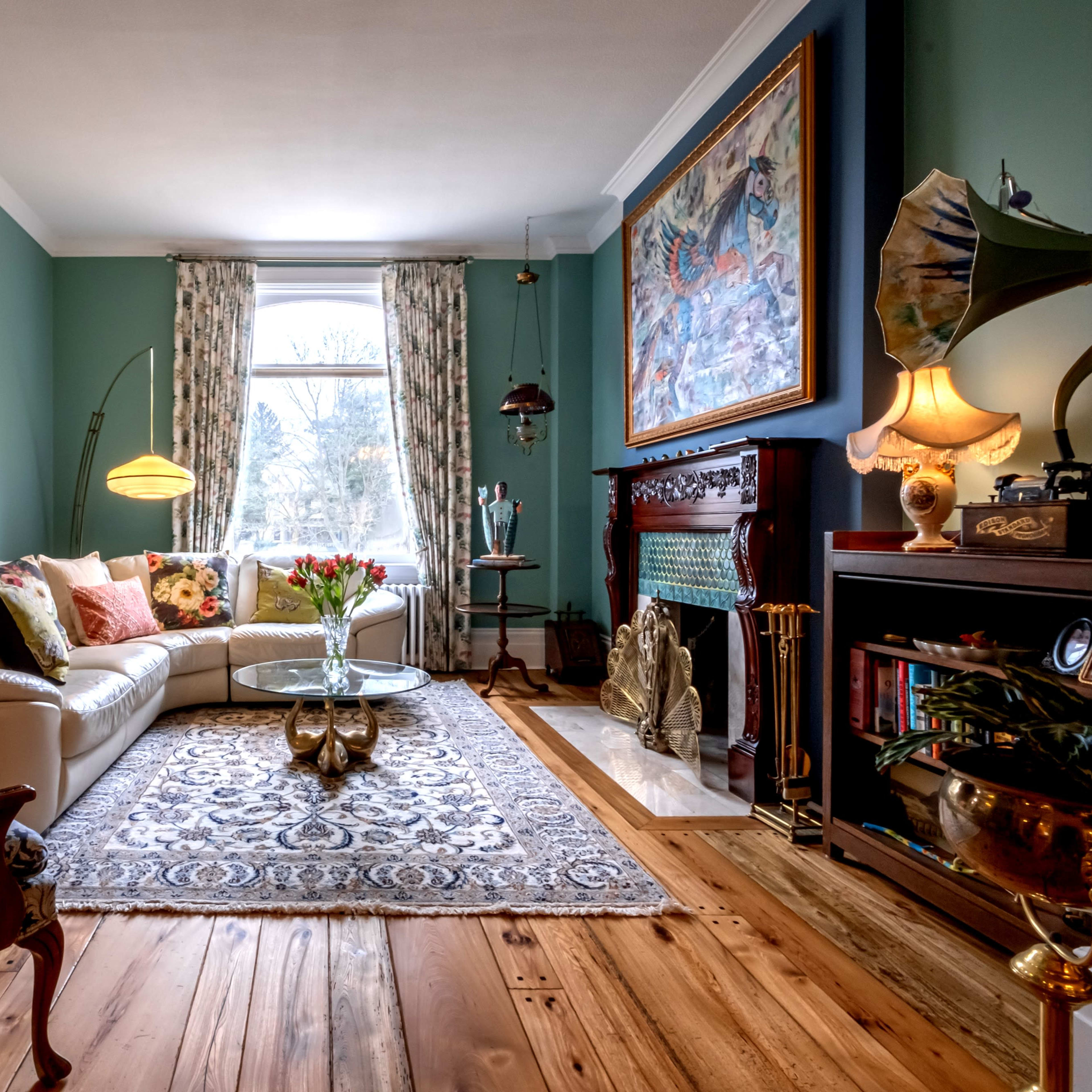 The living room features a cream-colored sofa, a glass coffee table, and a vintage fireplace, all set against a backdrop of teal walls and hardwood floors.