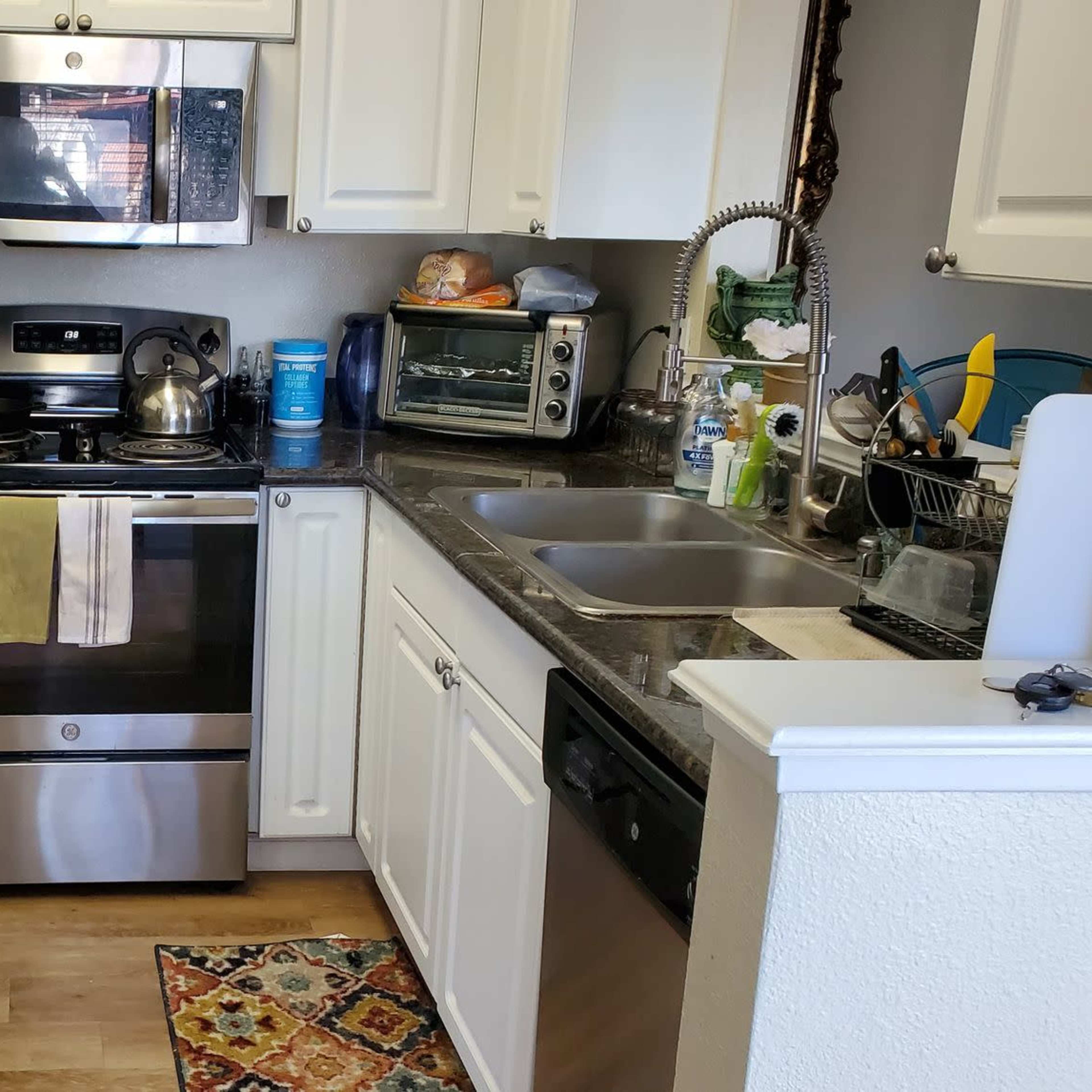 A kitchen featuring stainless steel appliances, white cabinetry, and a granite countertop, with a colorful rug on the floor.