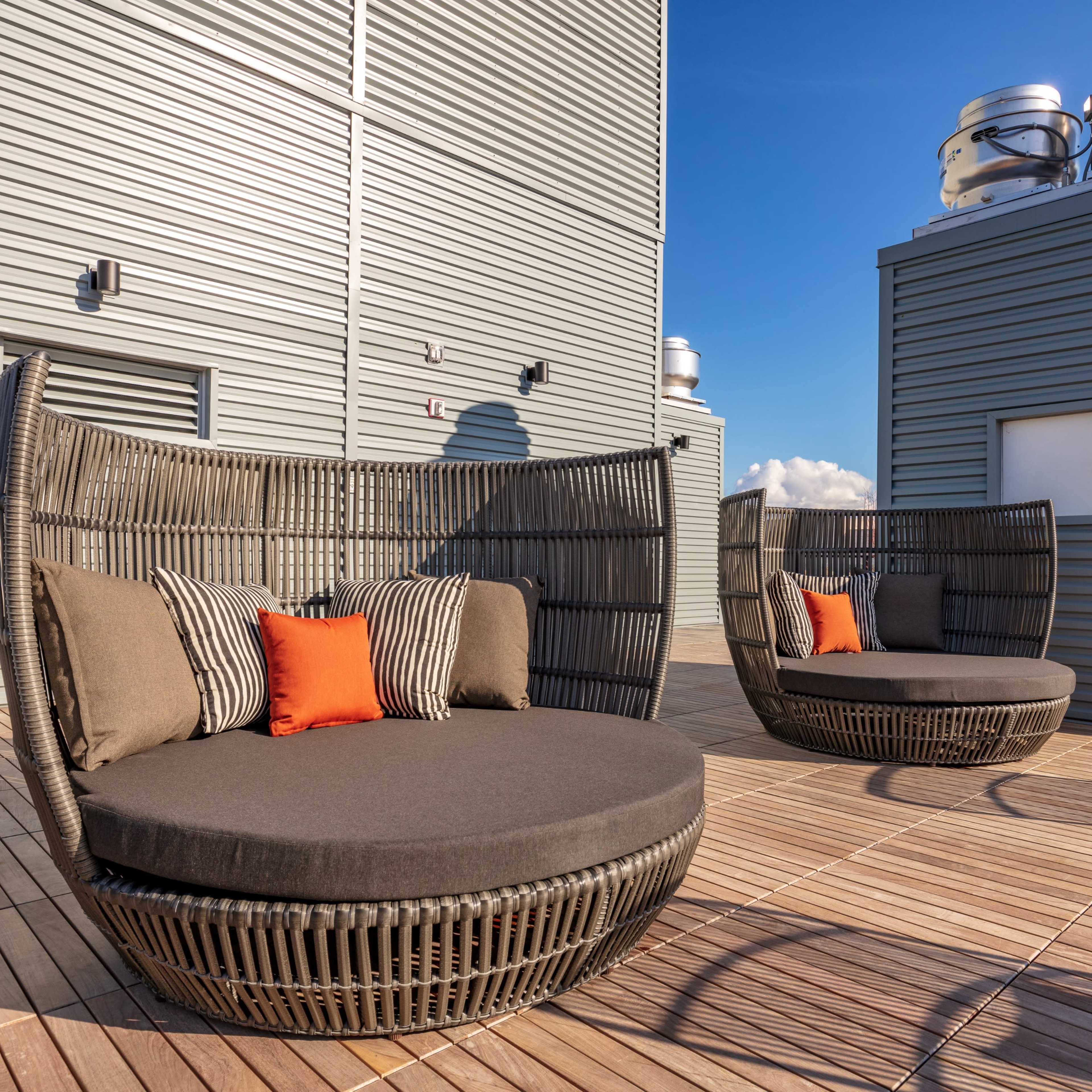 Two round, wicker lounge chairs with cushions, positioned on a wooden deck near gray building structures.