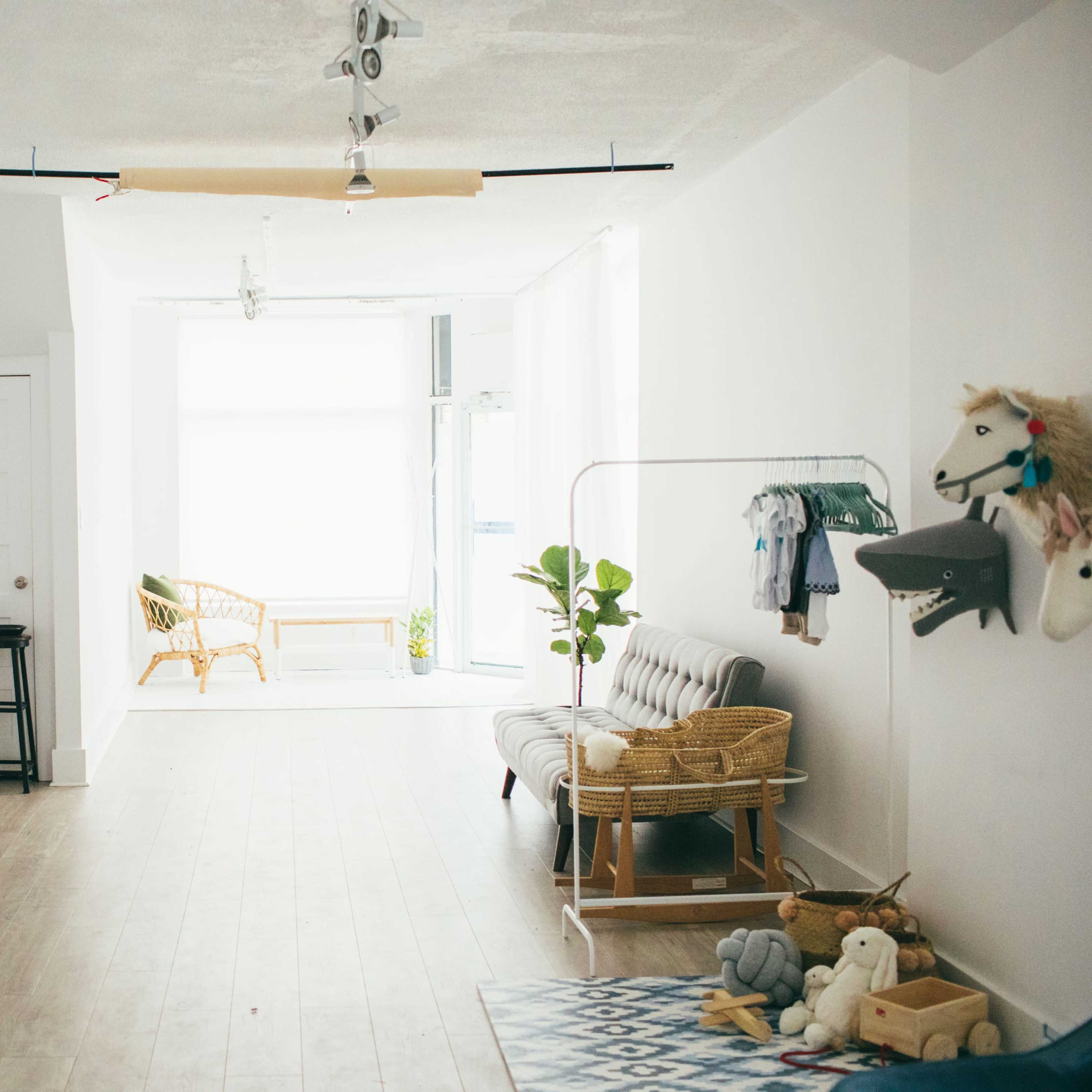 A bright, minimalist room with light wood flooring, featuring a seating area, a clothing rack, and various decor items on display.