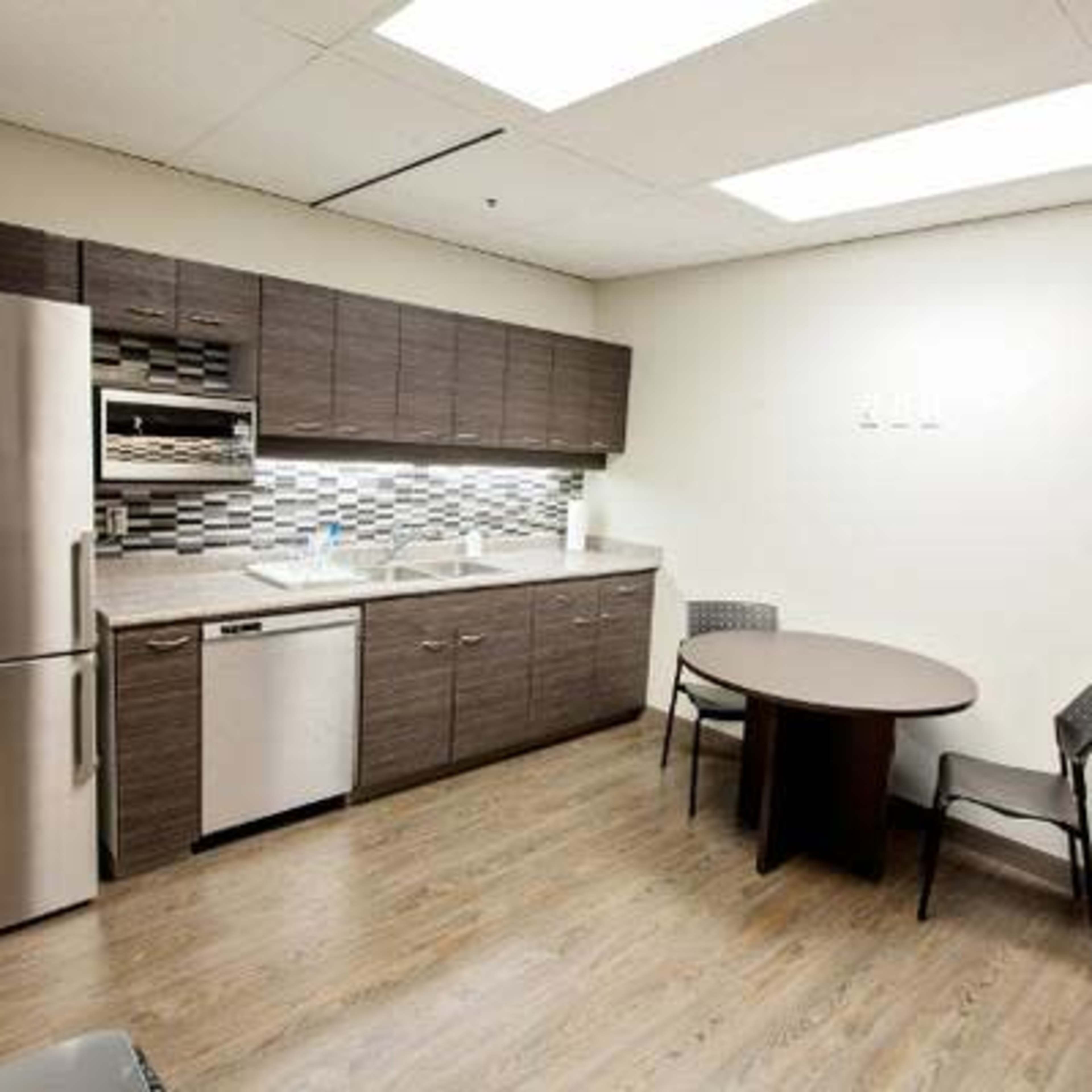 A modern kitchen with dark cabinets, stainless steel appliances, and a round table with chairs.