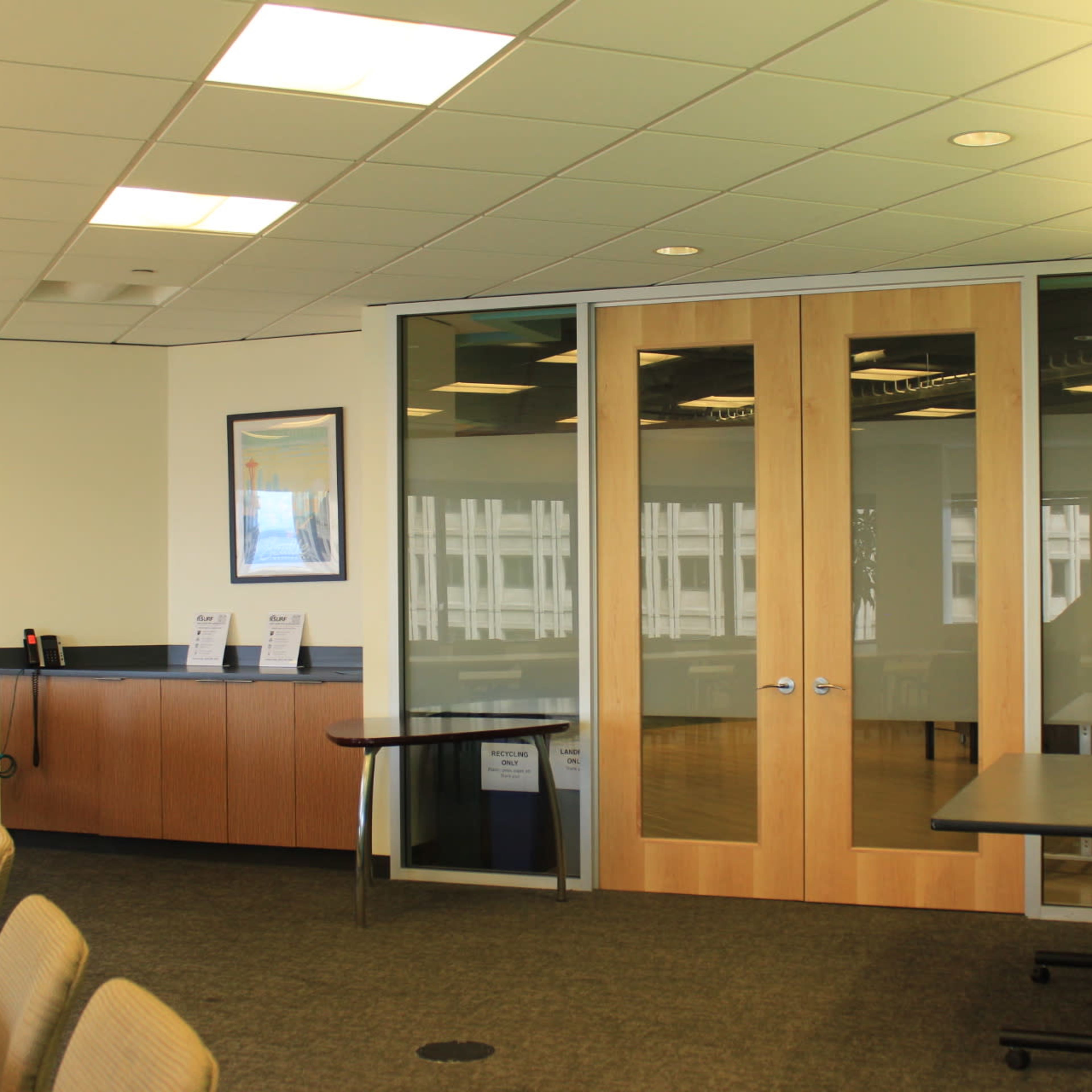 A modern conference room features glass doors, a long table with chairs, and a blue accent wall with a potted plant.