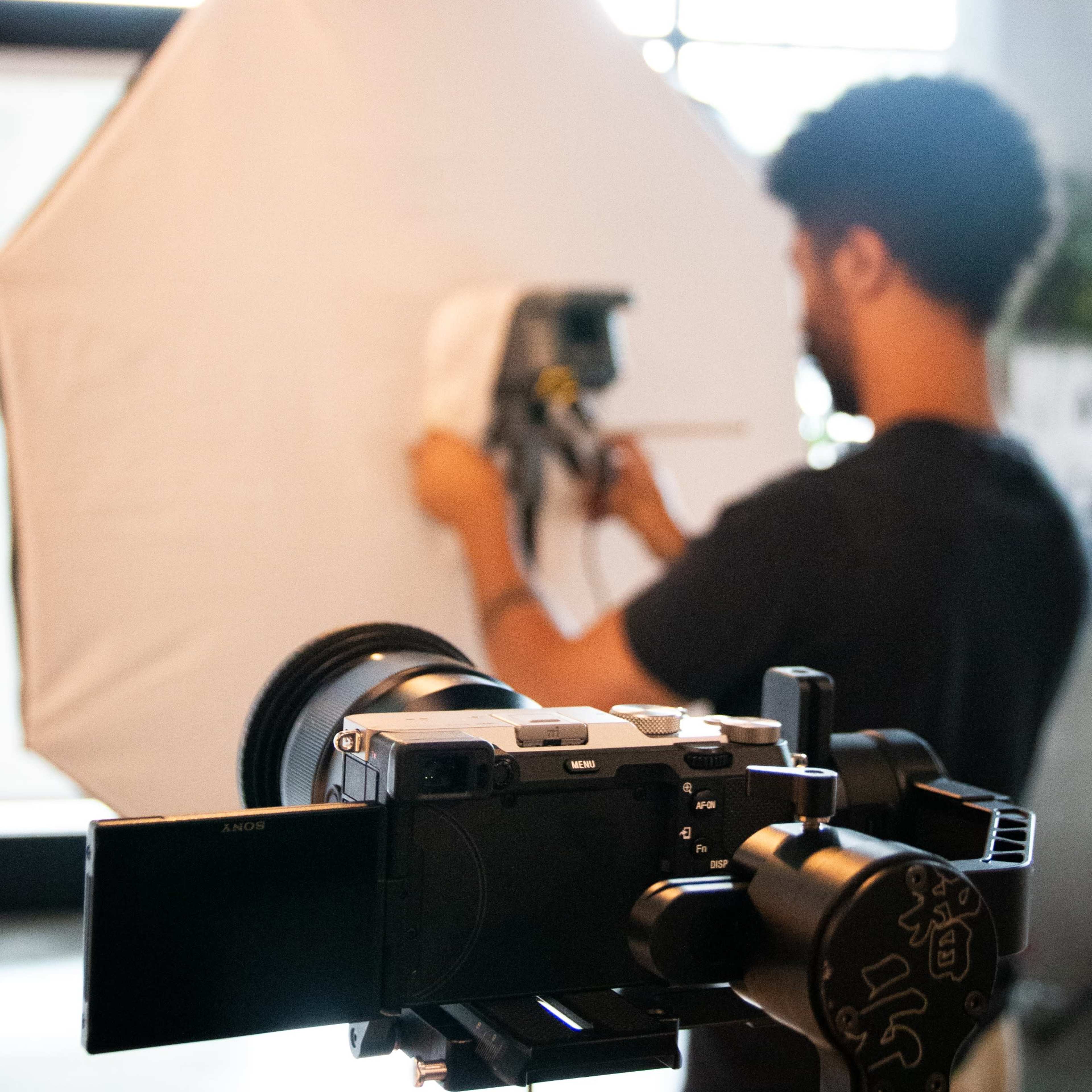 A person adjusts a lighting setup with a large softbox while a camera is positioned in the foreground.