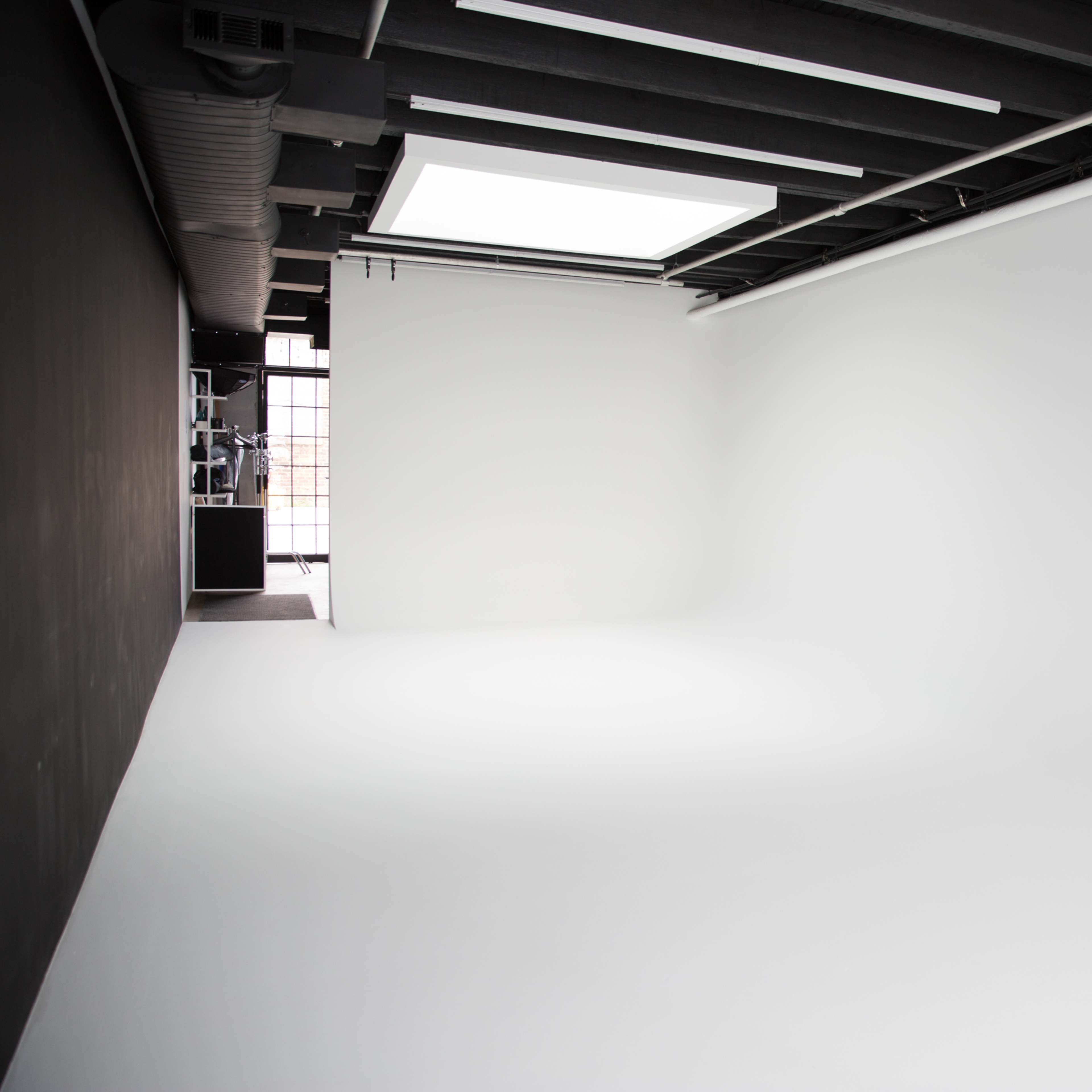 A spacious, empty photography studio with white walls and a large window letting in natural light.