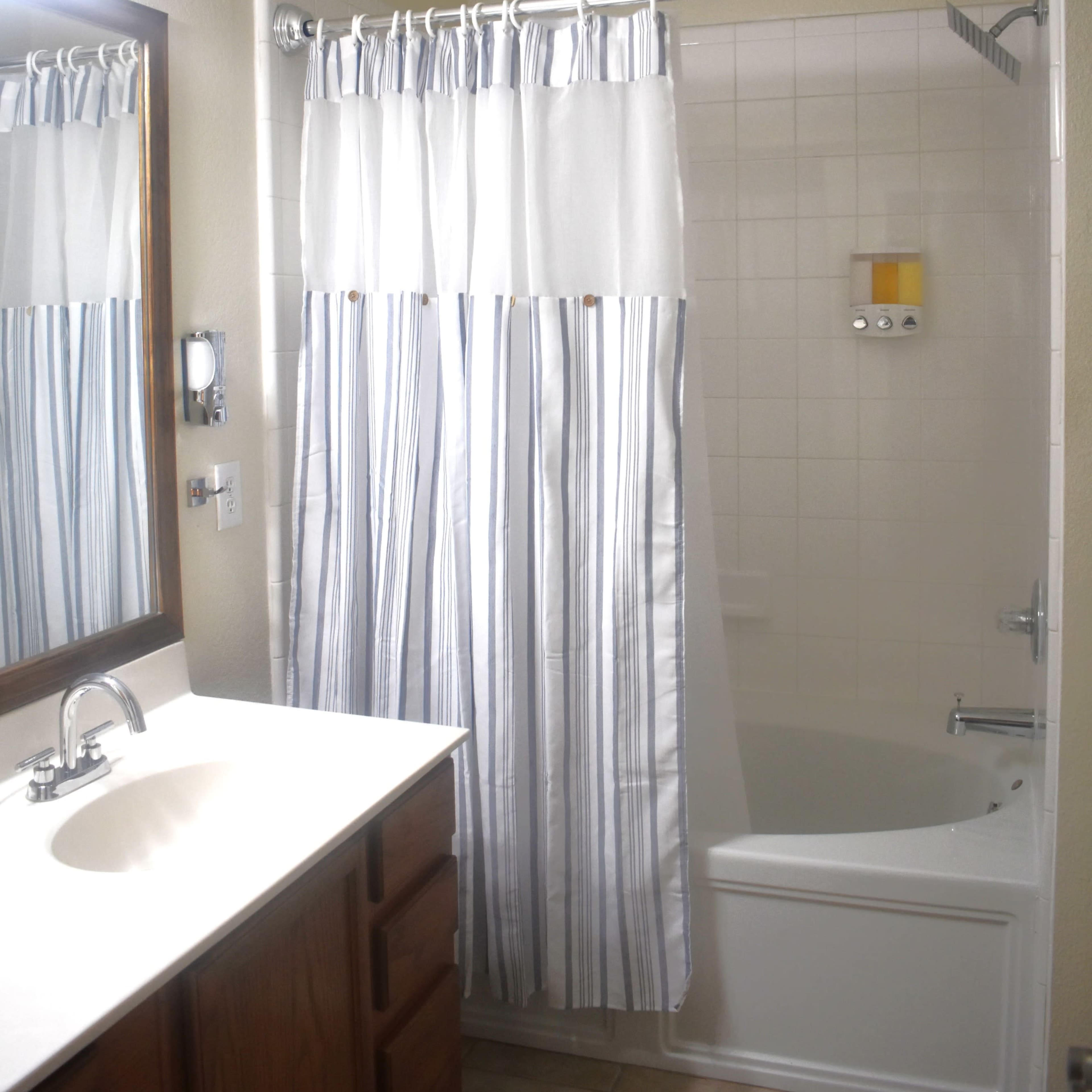 A bathroom with a bathtub, a shower curtain with stripes, a mirror above the sink, and wooden cabinets.