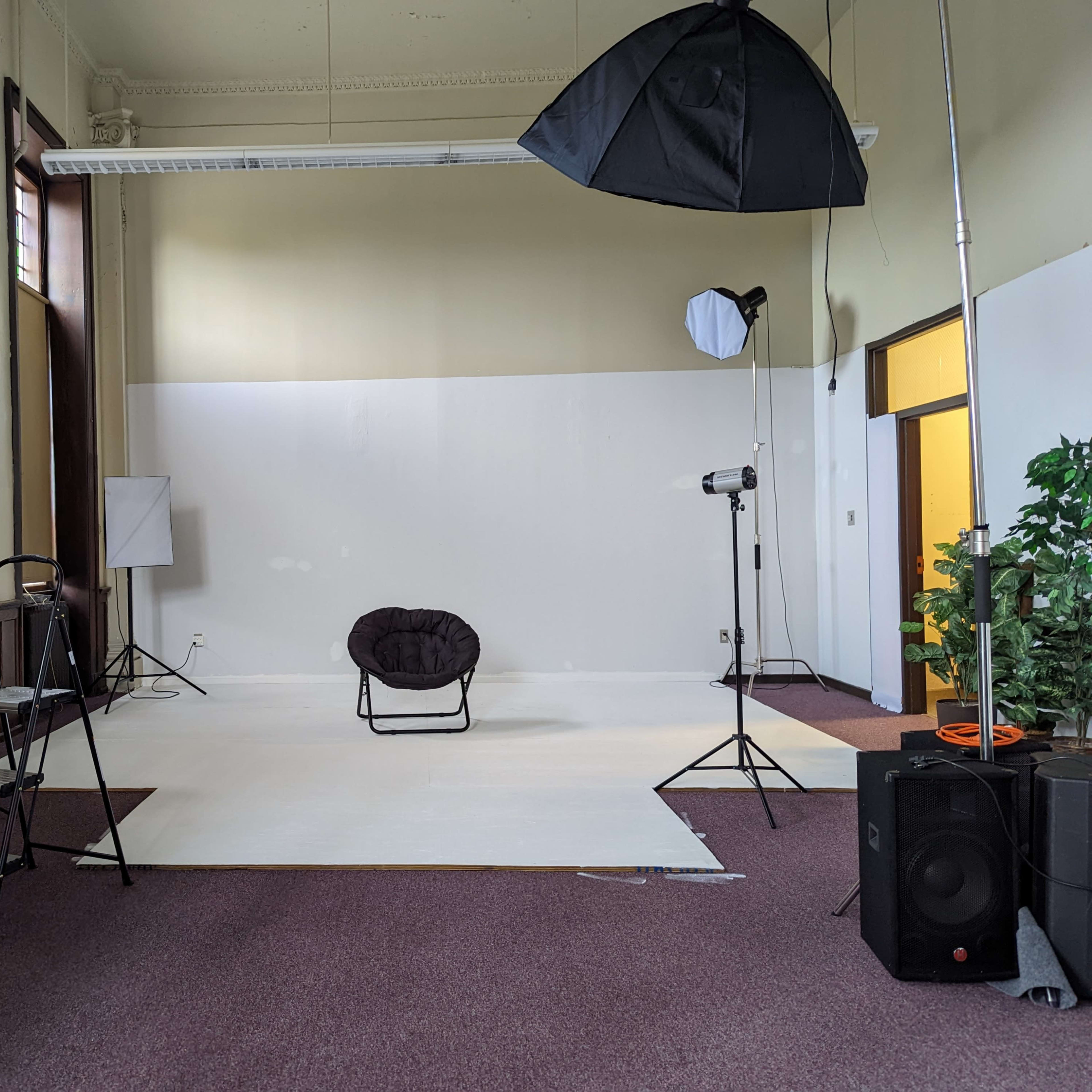 An empty photography studio equipped with a chair, lighting equipment, and backdrops.
