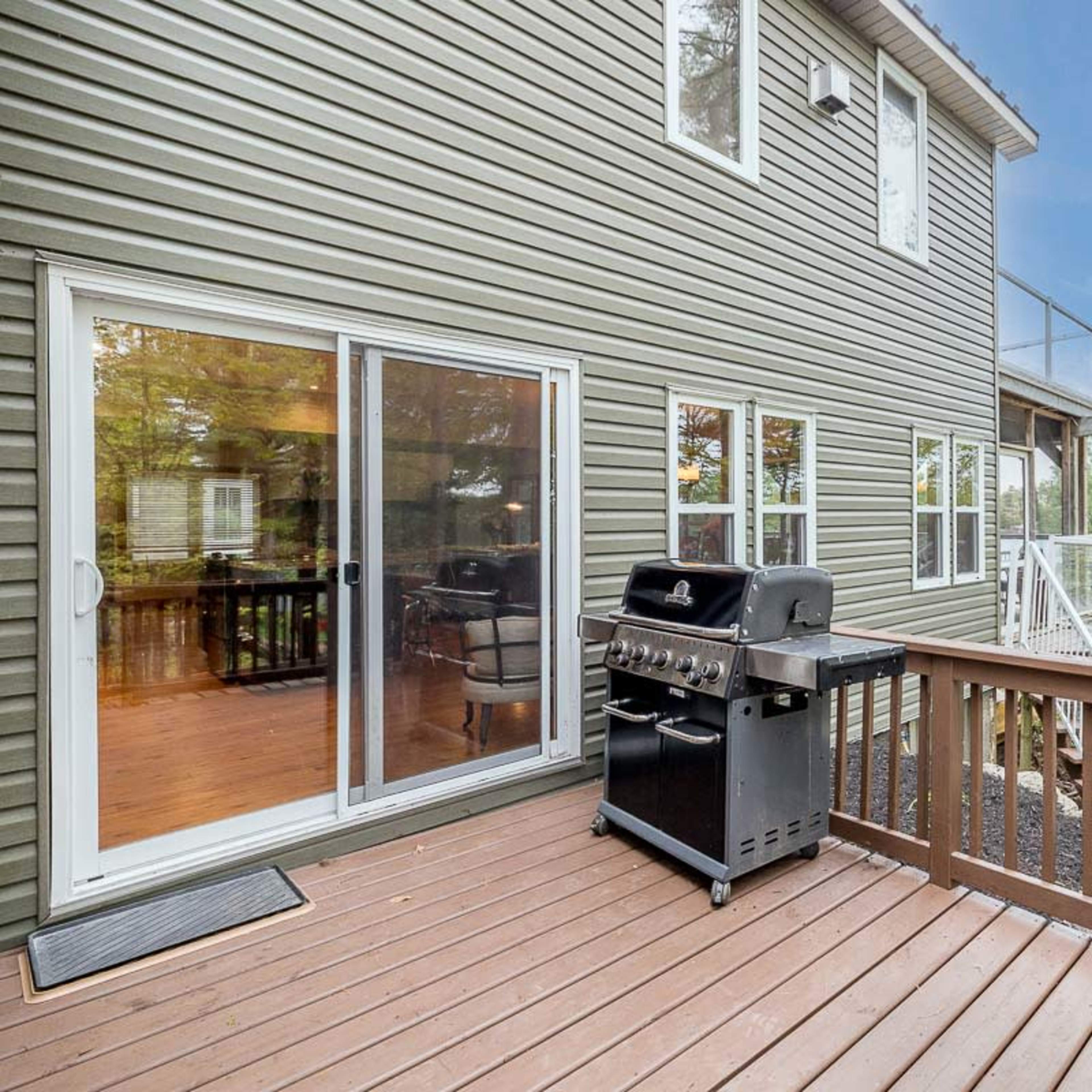 A wooden deck features a barbecue grill and provides a view of the water through large sliding glass doors.