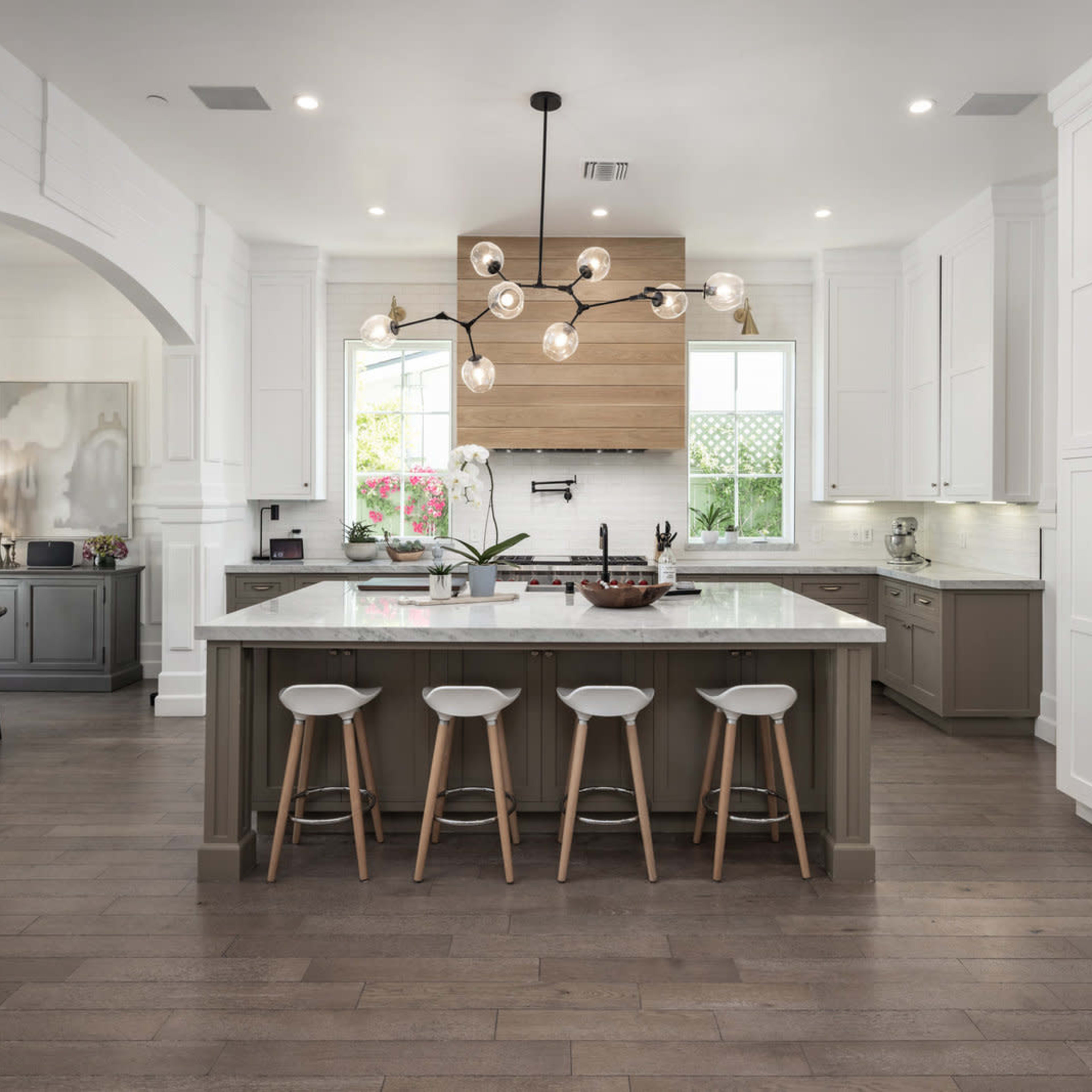 A modern kitchen with a central island, pendant lighting, and white cabinetry, featuring a mix of dark and light wood elements.