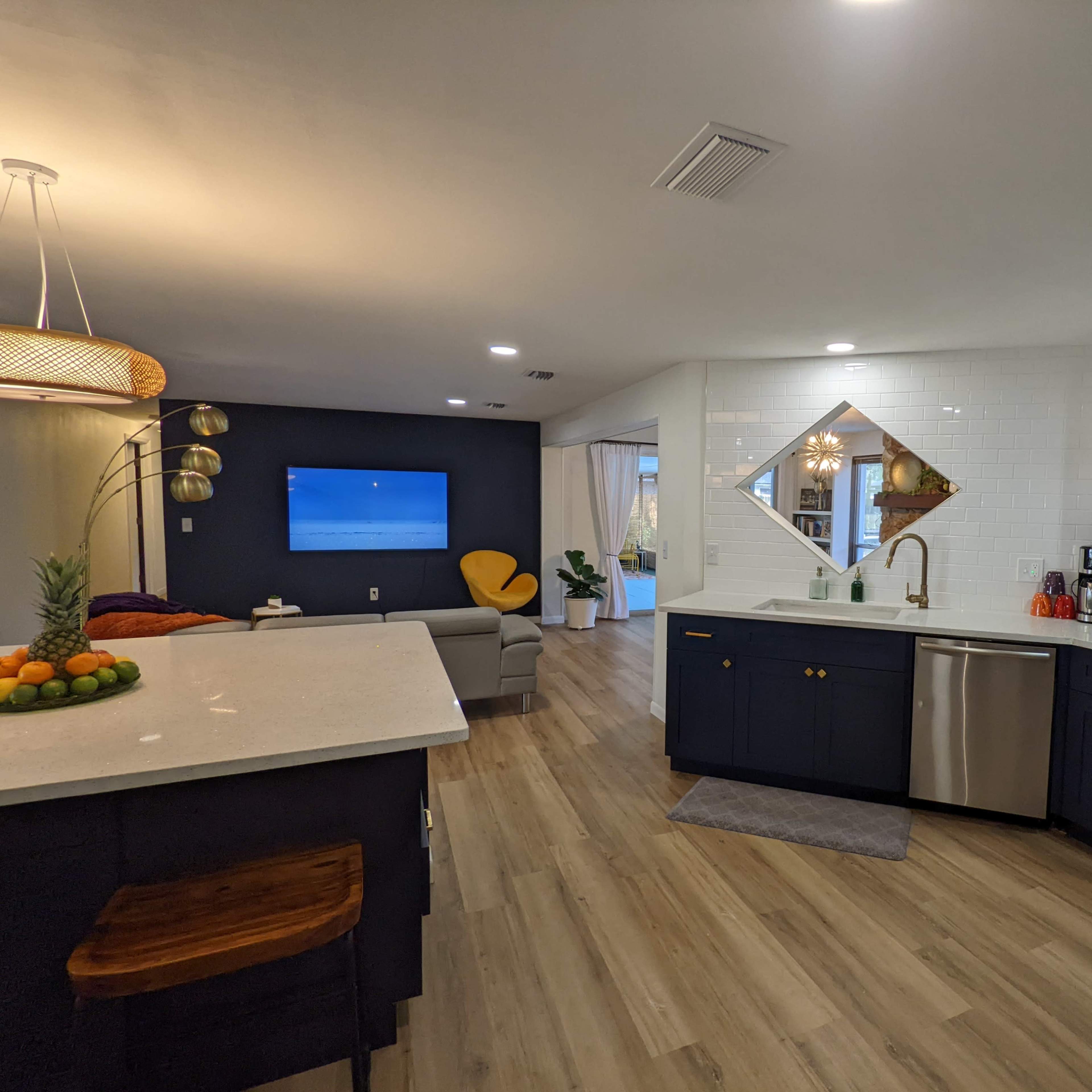 A modern kitchen with navy blue cabinets, a stainless steel sink, and a living area featuring a television and a gray sofa.