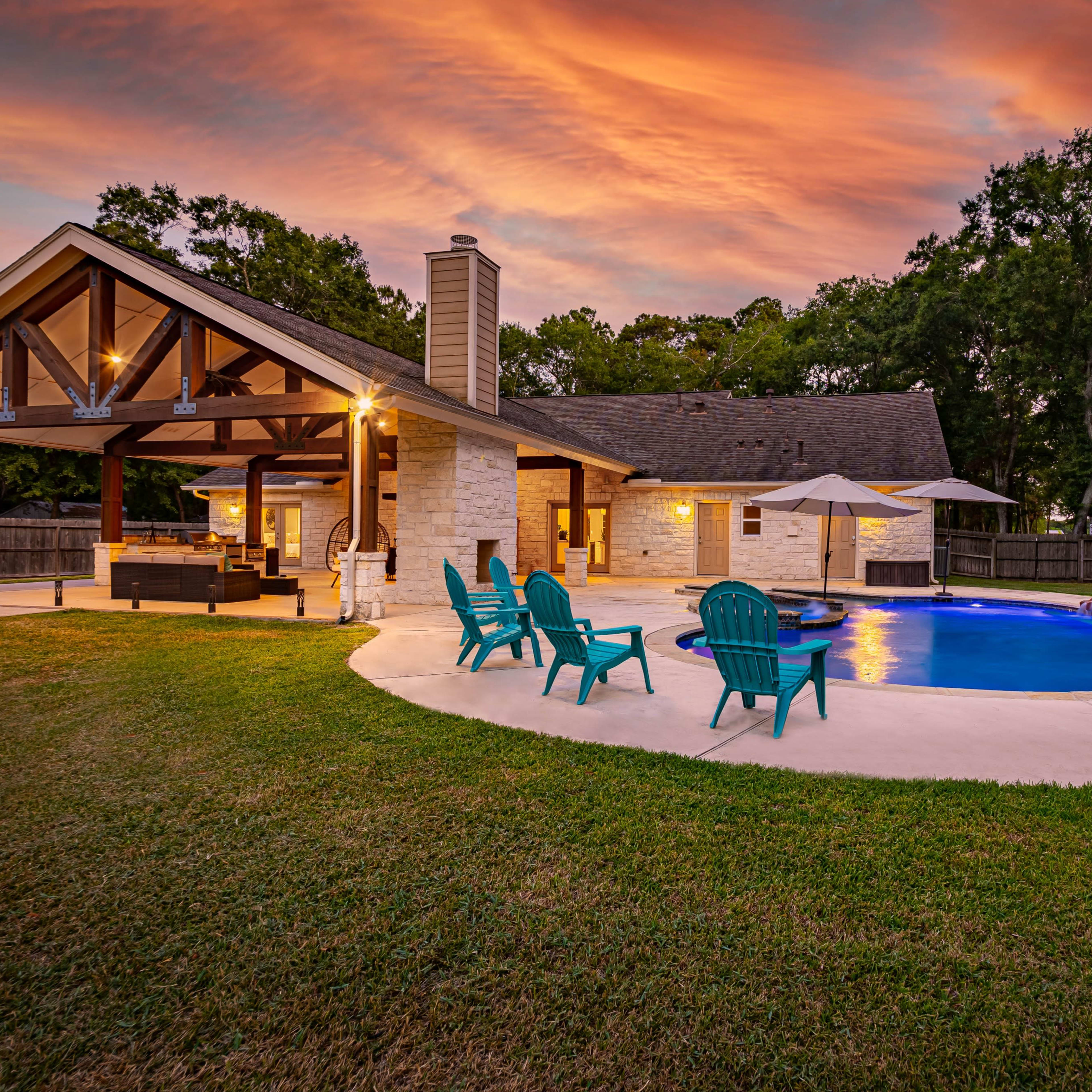 A backyard with a swimming pool, lounge chairs, and a covered patio, set against a colorful sunset sky.