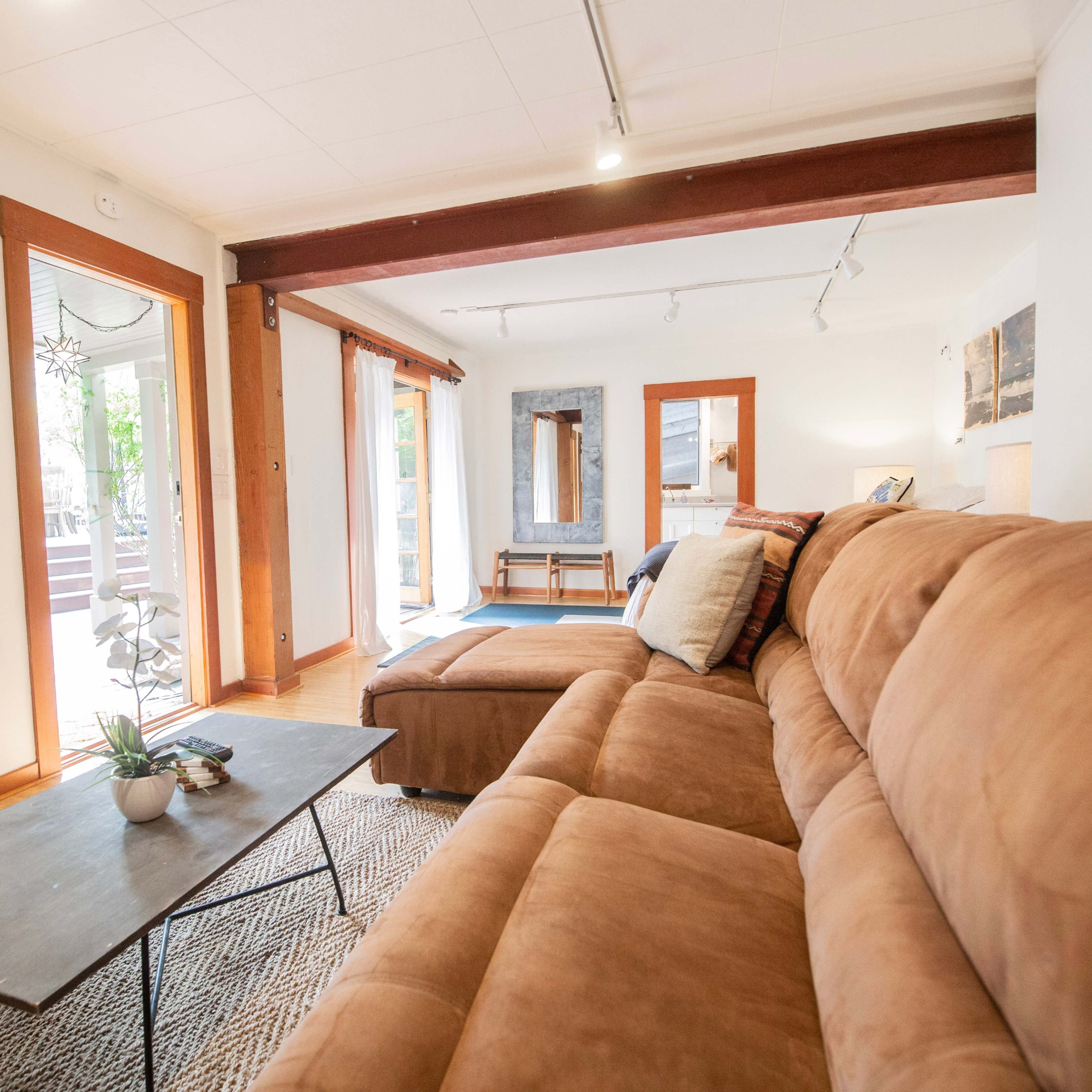 A spacious living room features a brown sectional sofa, a coffee table, and large windows letting in natural light.