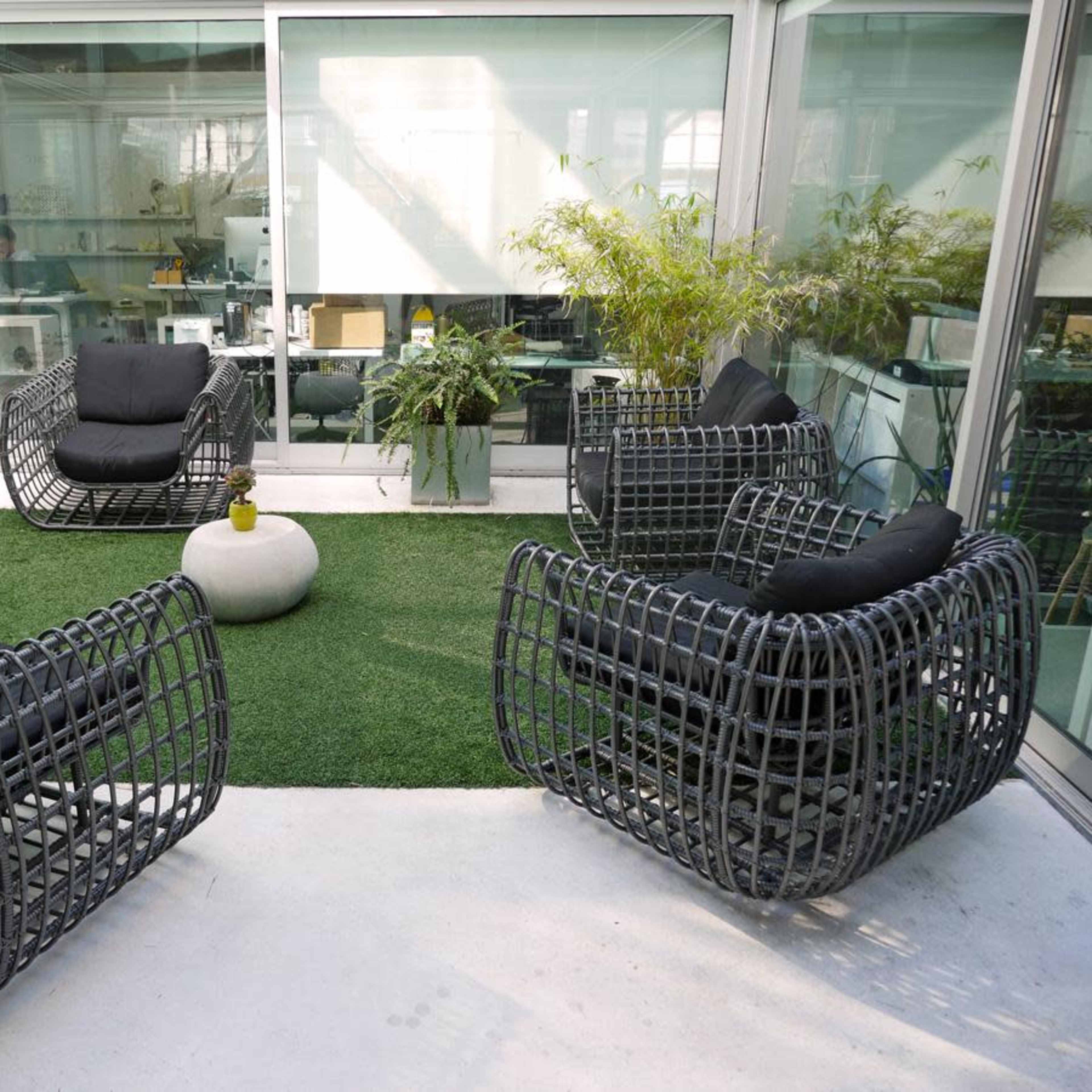 A modern indoor seating area with four woven chairs arranged around a circular stone table on artificial grass.