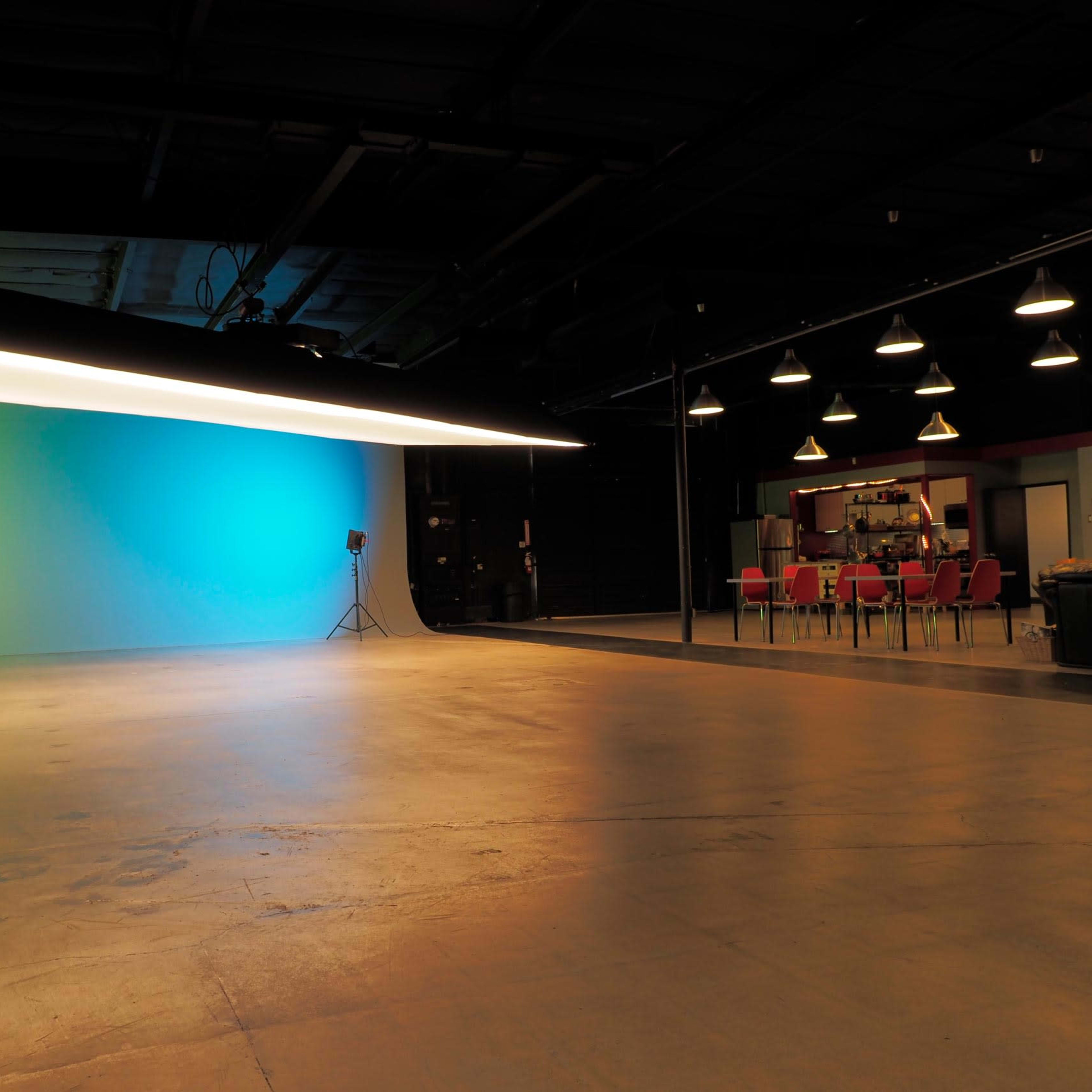 An empty studio space with a bright, colored backdrop and a dining area in the background.