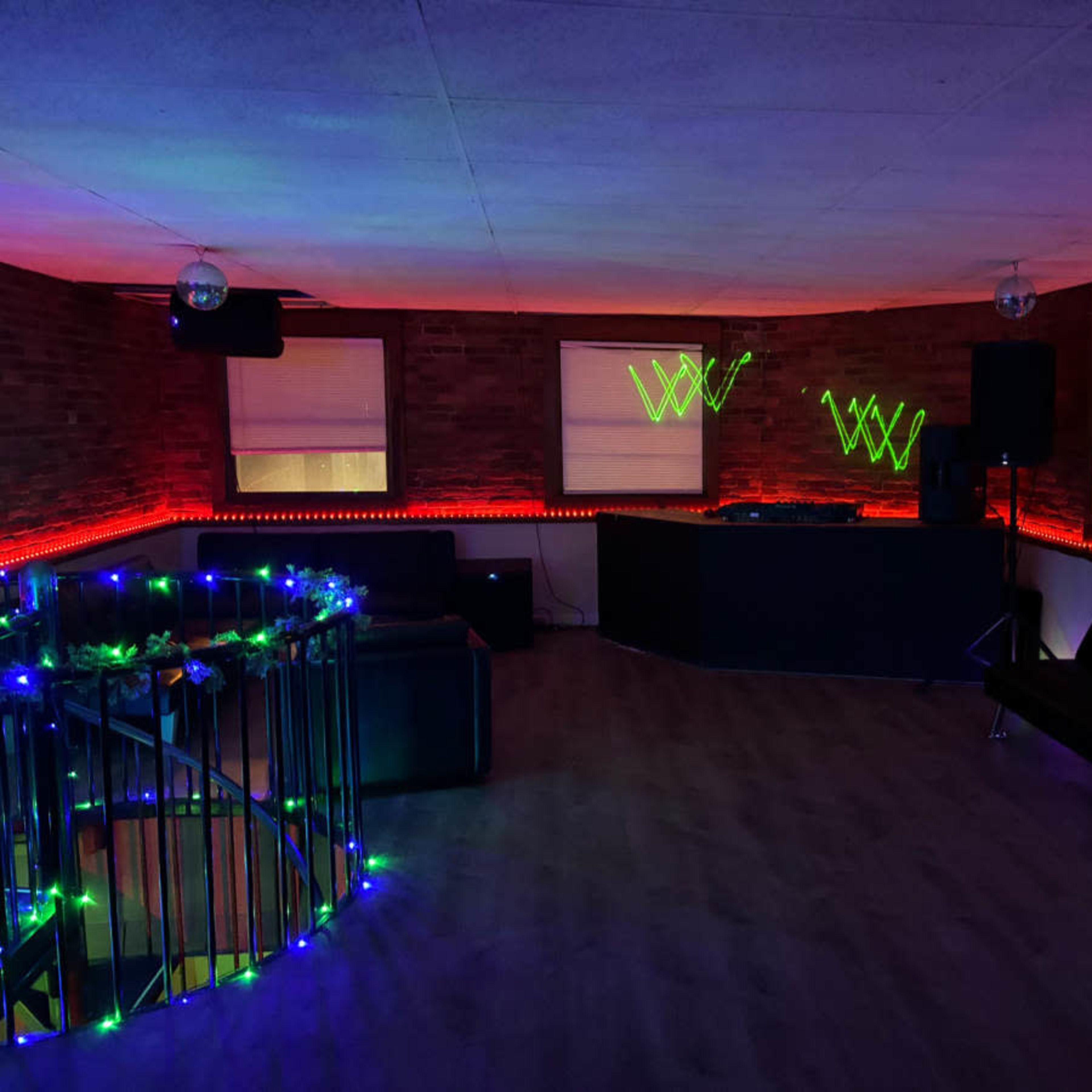 A dimly lit room with colorful LED lights accentuating a DJ booth and seating areas.