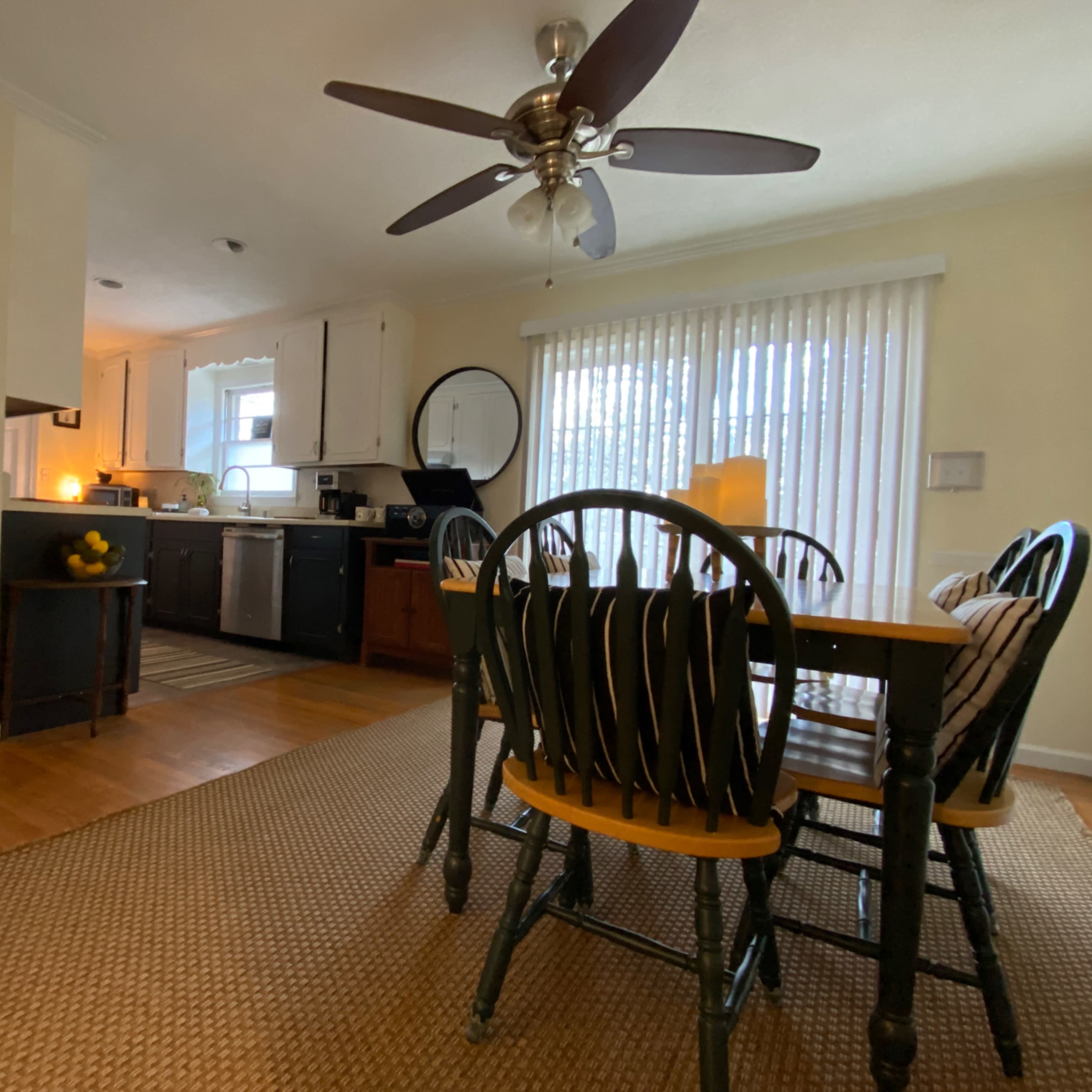 A dining area with a wooden table and six chairs, adjacent to a kitchen featuring light-colored cabinets and kitchen appliances.
