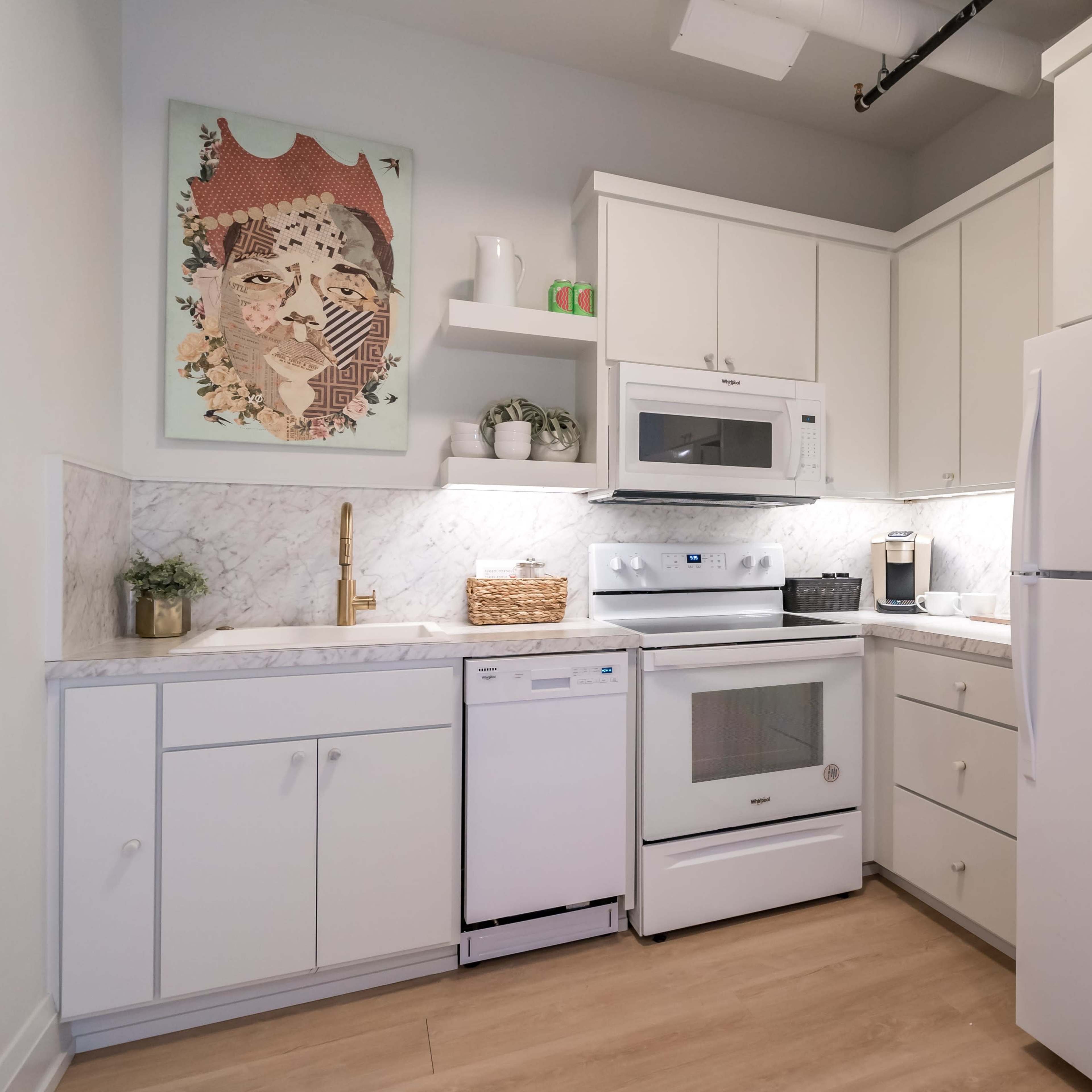 A compact kitchen features white cabinets, a marble backsplash, and modern appliances, including a refrigerator, stove, and dishwasher.