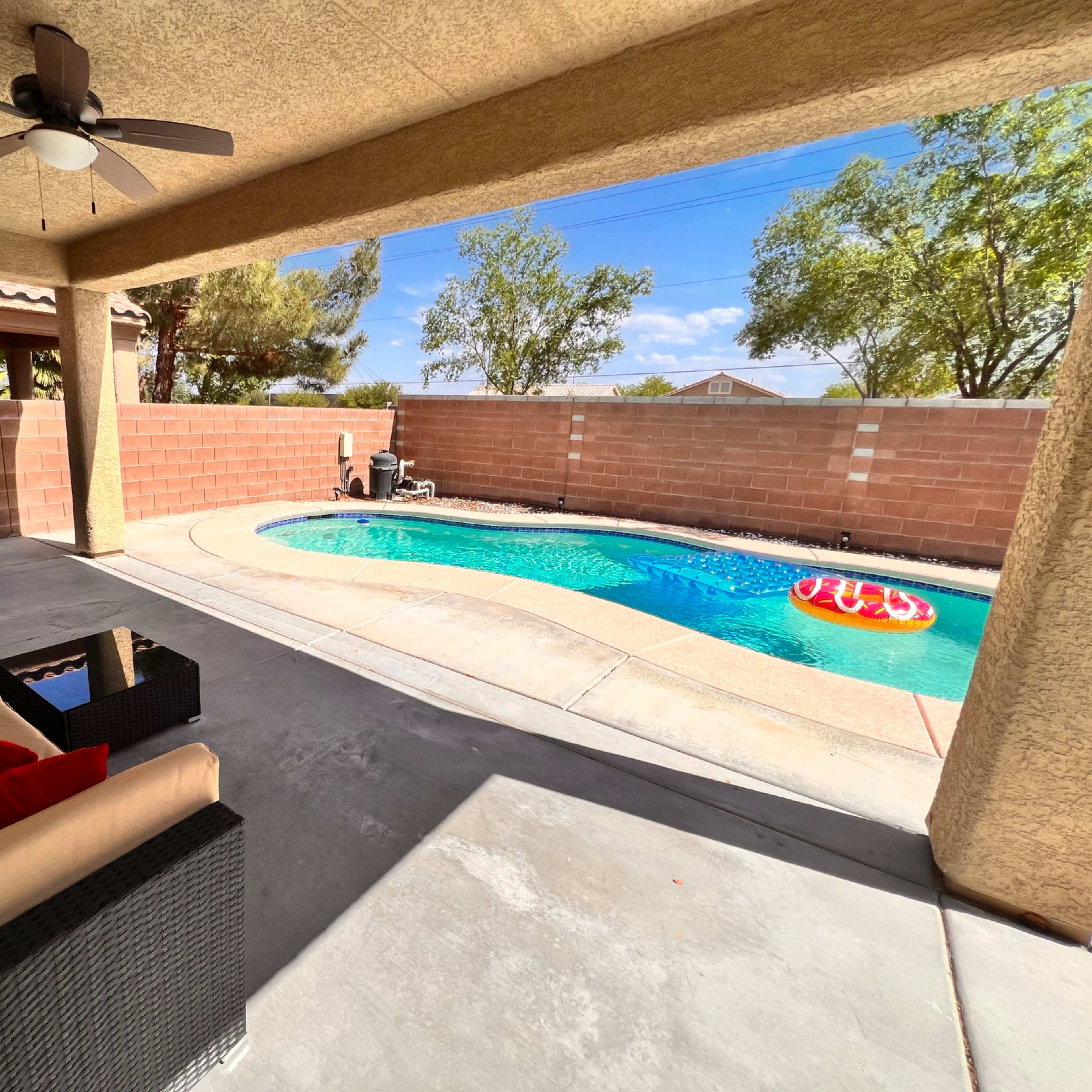A covered patio features a seating area and overlooks a swimming pool enclosed by a brick wall.