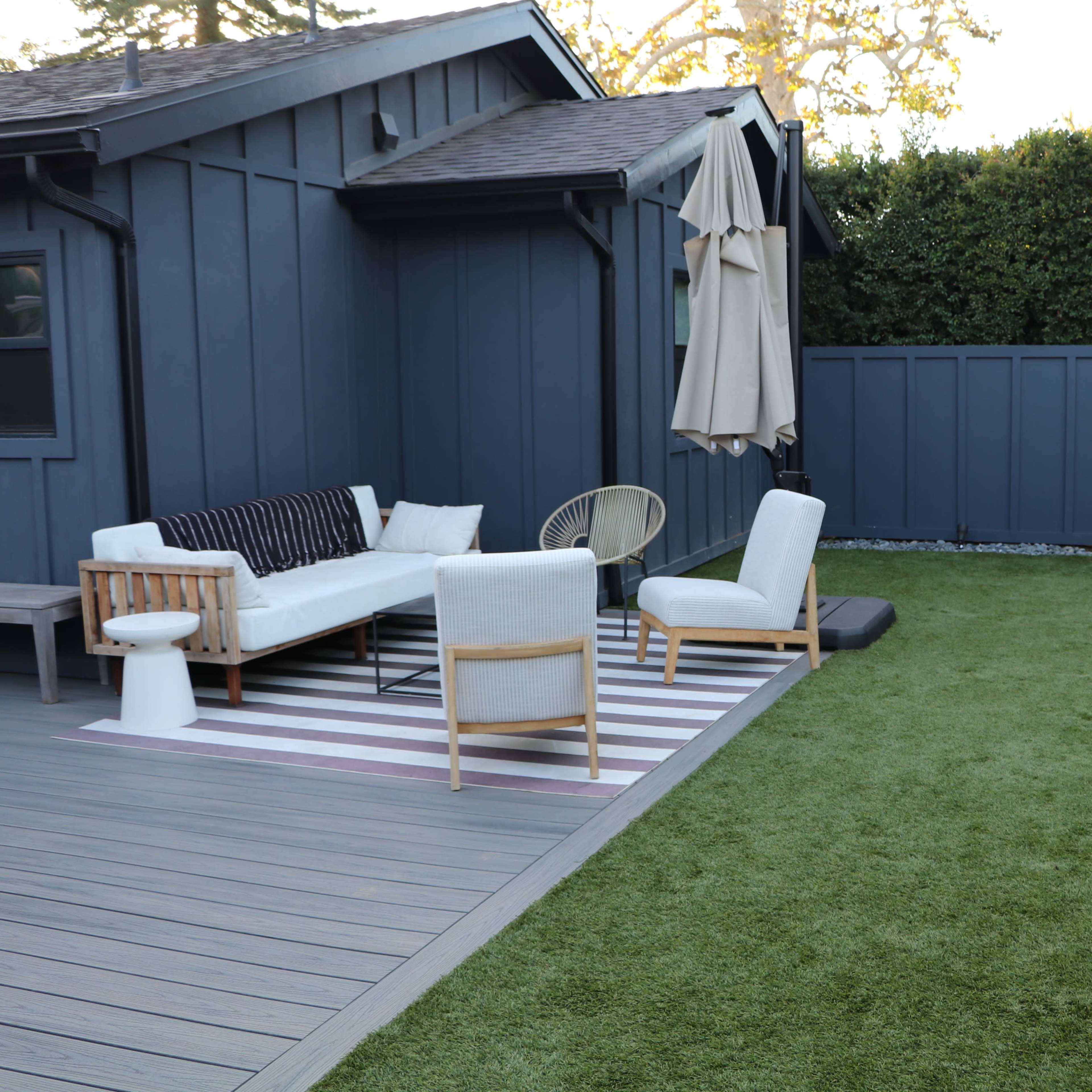A patio area with a furniture set, an umbrella, and artificial grass surrounded by a fence.