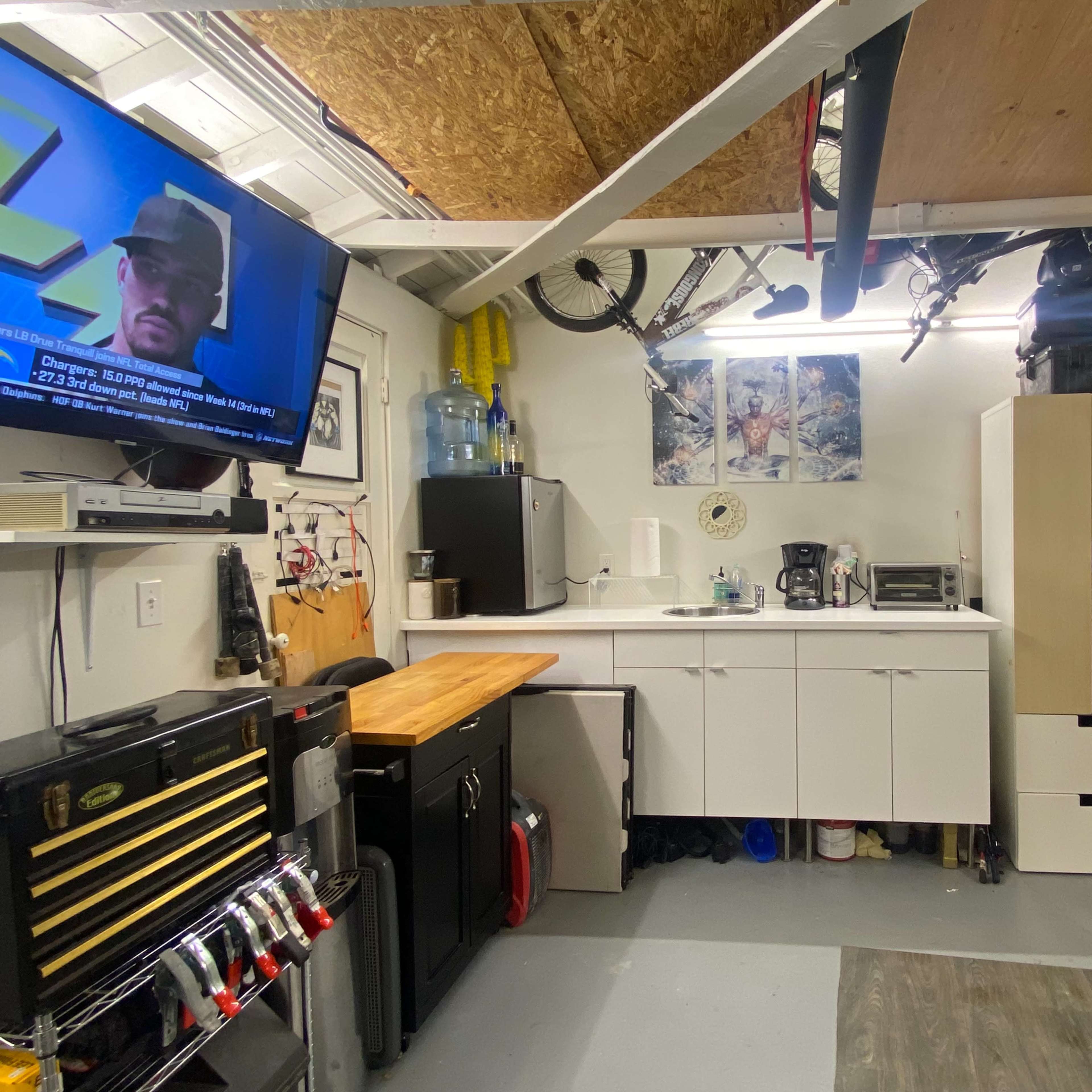 A garage workspace with a counter, various appliances, storage cabinets, tools, and bicycles hanging from the ceiling.
