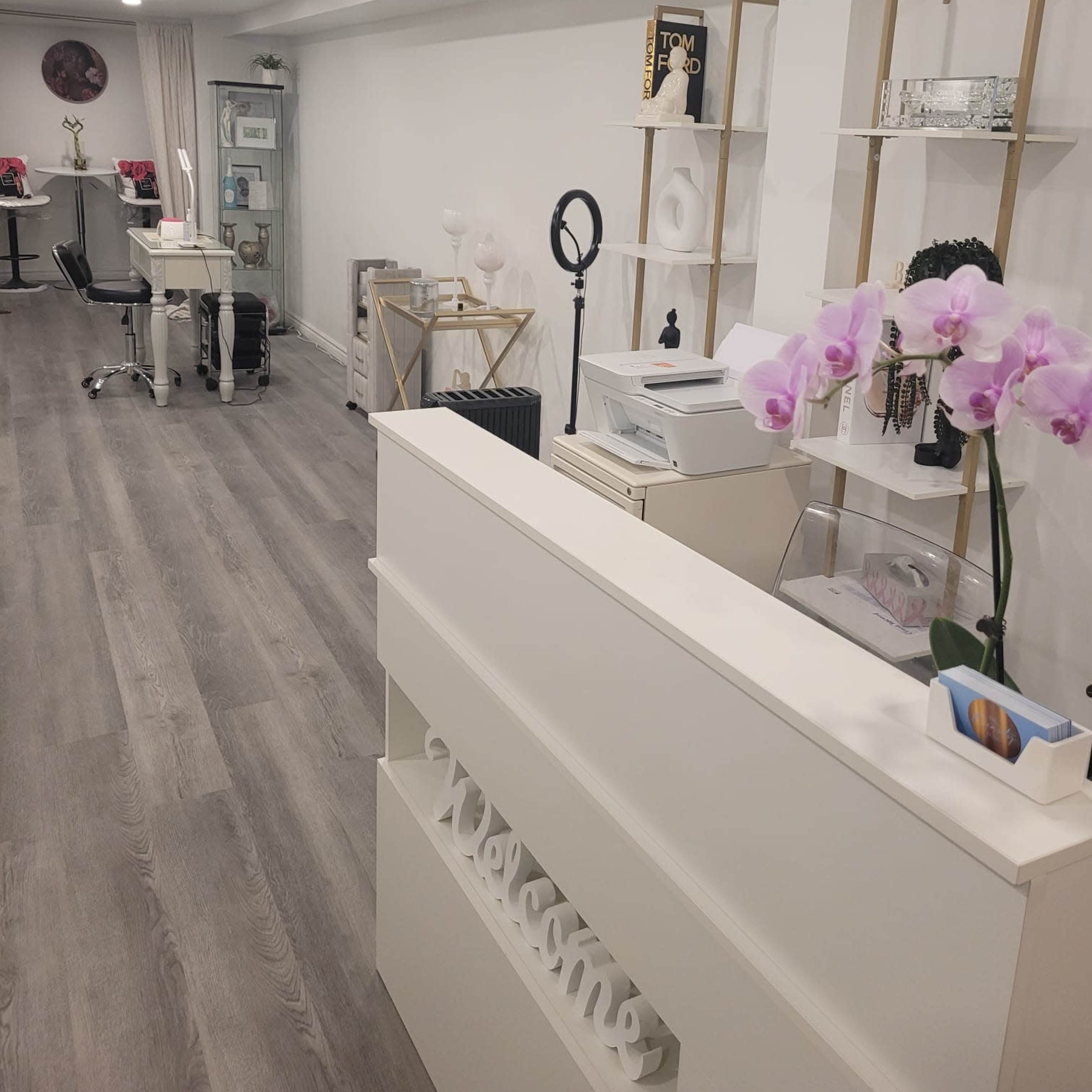 A modern reception area with a white desk, decorative shelves, and a setup for beauty services.