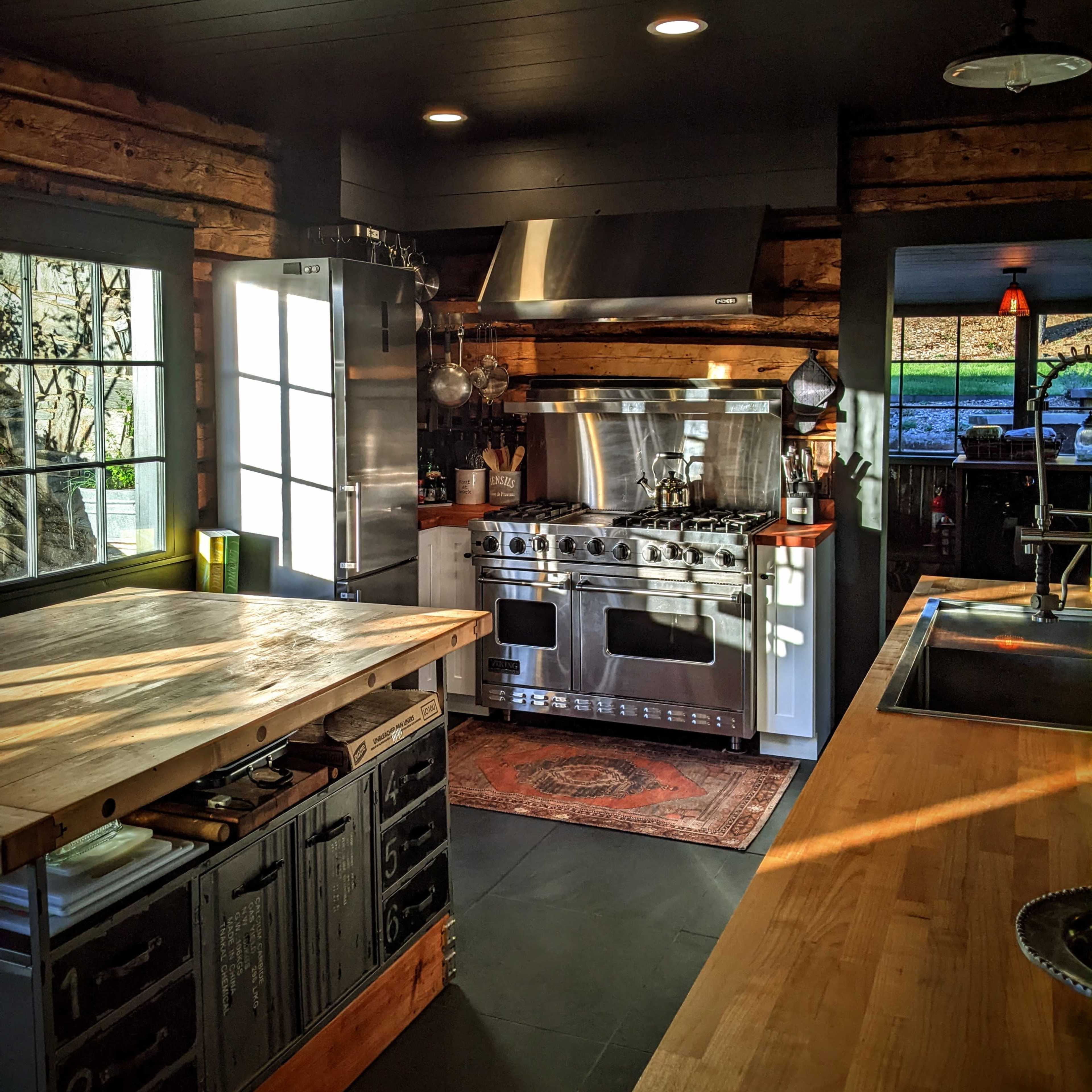 A modern kitchen with stainless steel appliances, a wooden island, and large windows allowing natural light to enter.