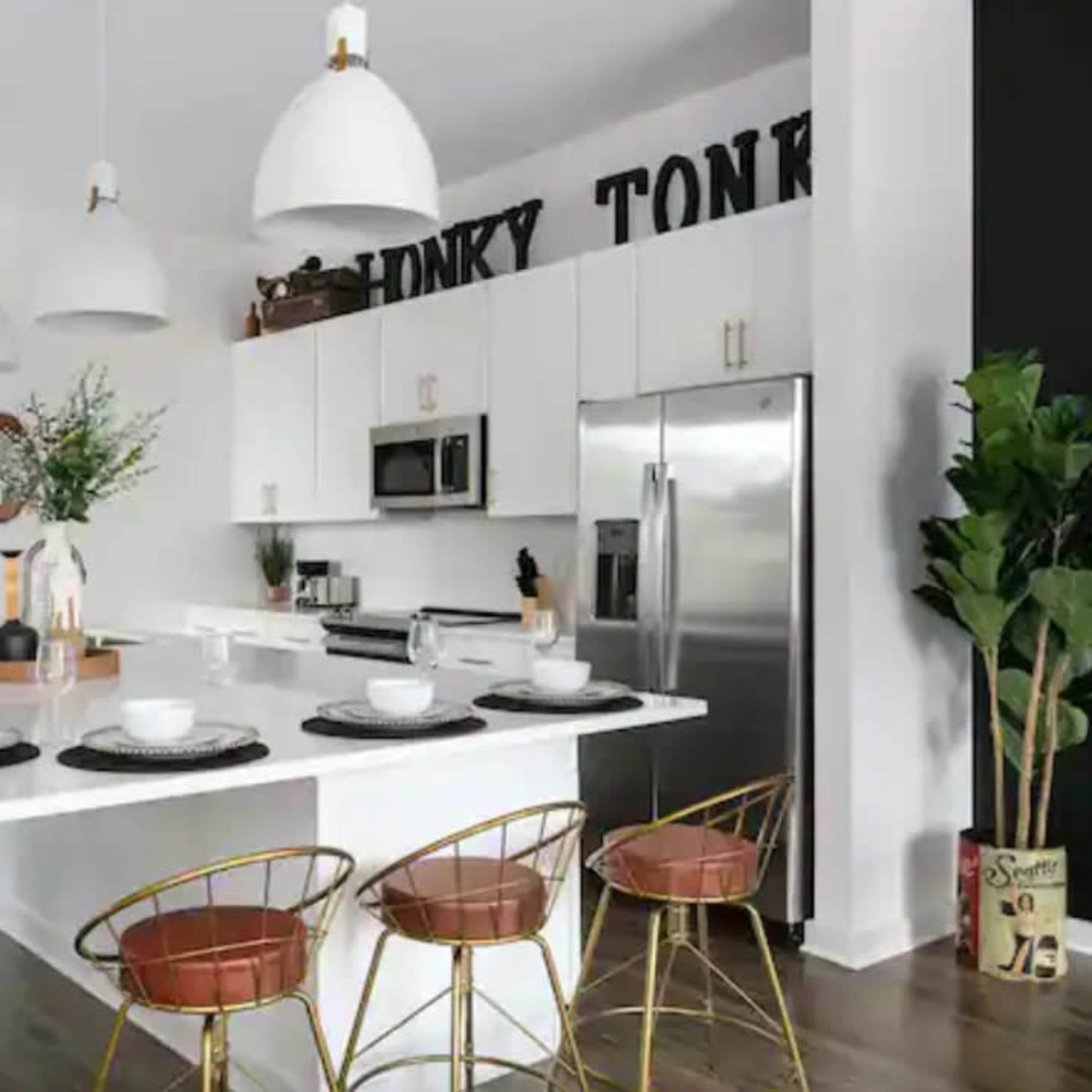 A modern kitchen features white cabinetry, stainless steel appliances, a large island with bar seating, and decorative elements on the walls.