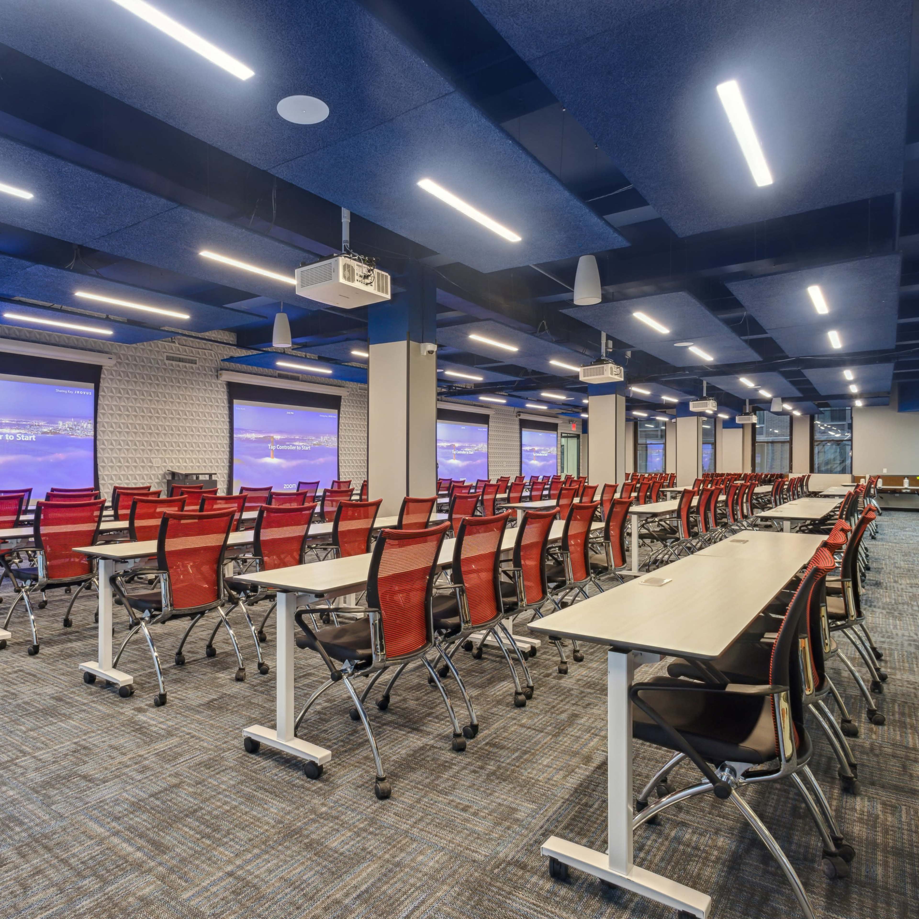 A modern conference room set up with rows of tables and chairs facing two projection screens.