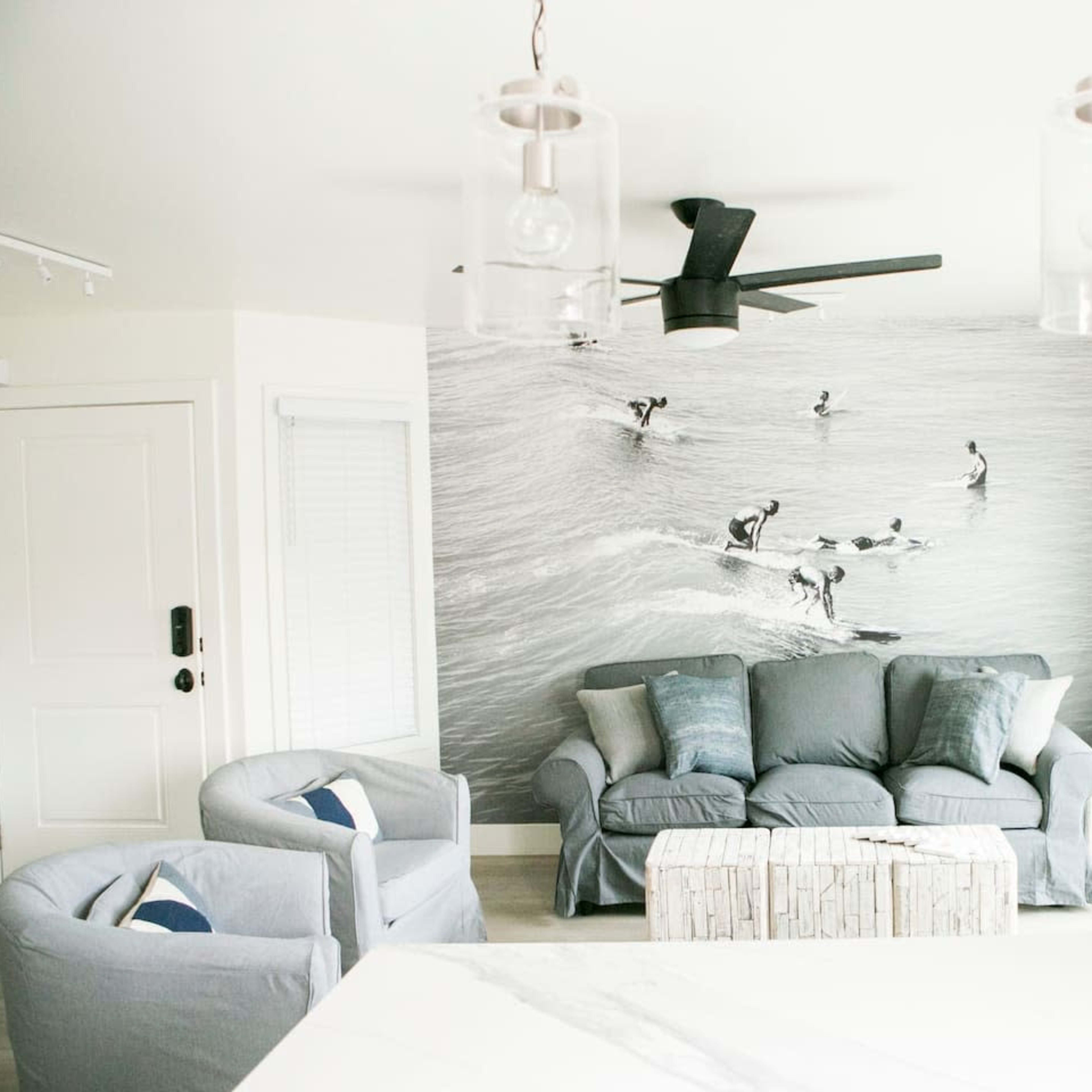 A living room with a surf-themed mural, gray sofas, and light-colored wooden furniture.