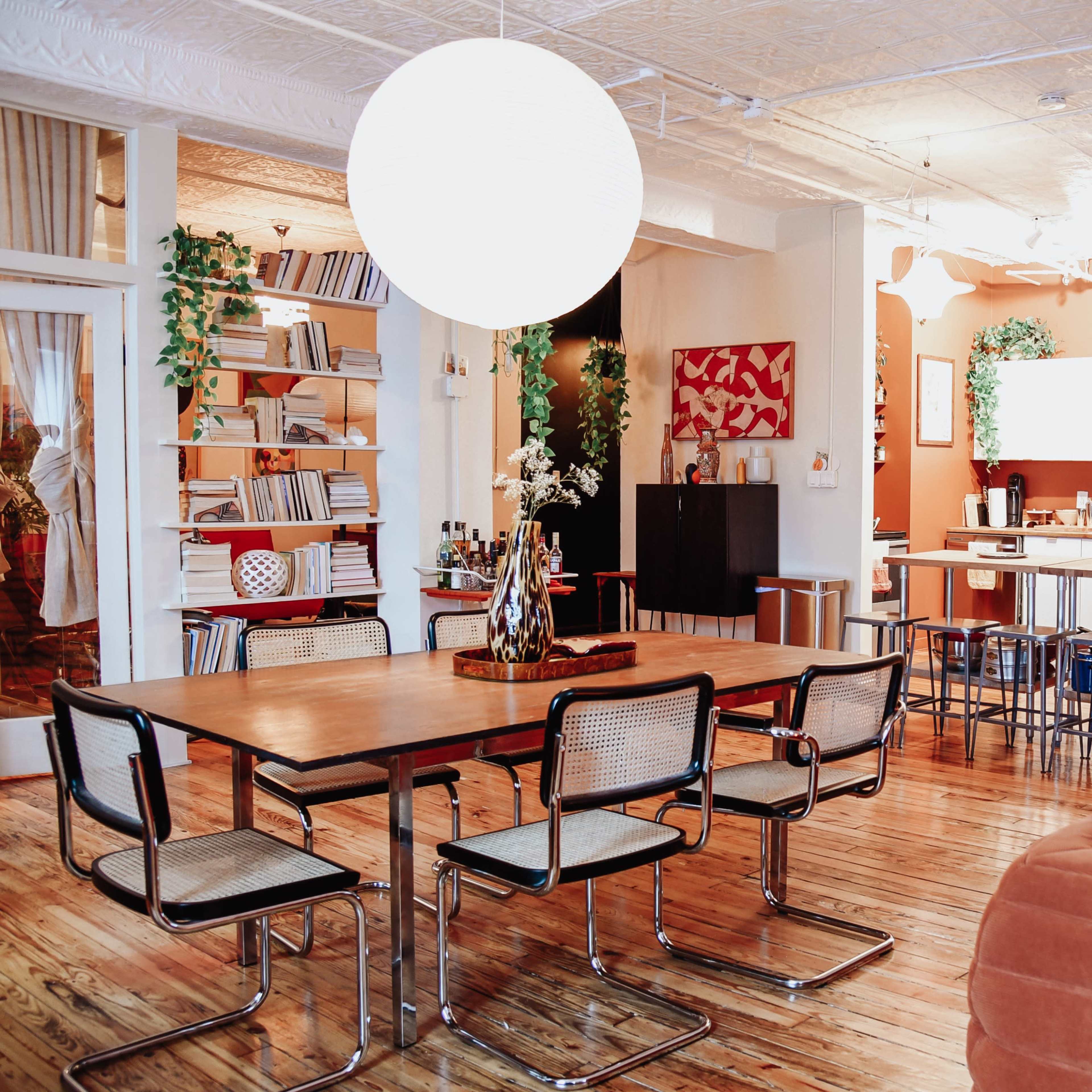 A spacious living area with a wooden dining table, modern chairs, a cozy sofa, and an open kitchen visible in the background.
