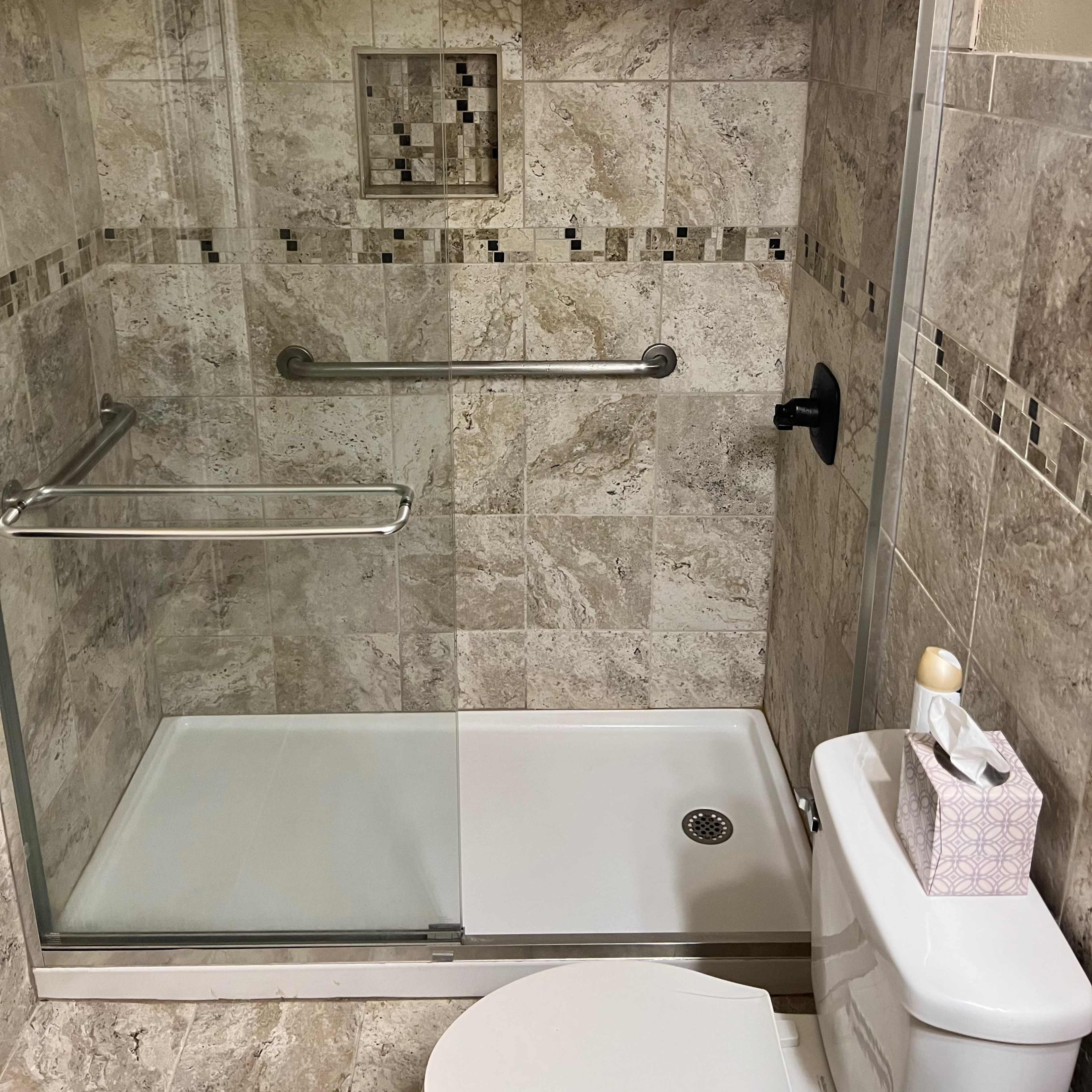 A tiled shower area with a glass door, a wall-mounted grab bar, and a toilet adjacent to it.