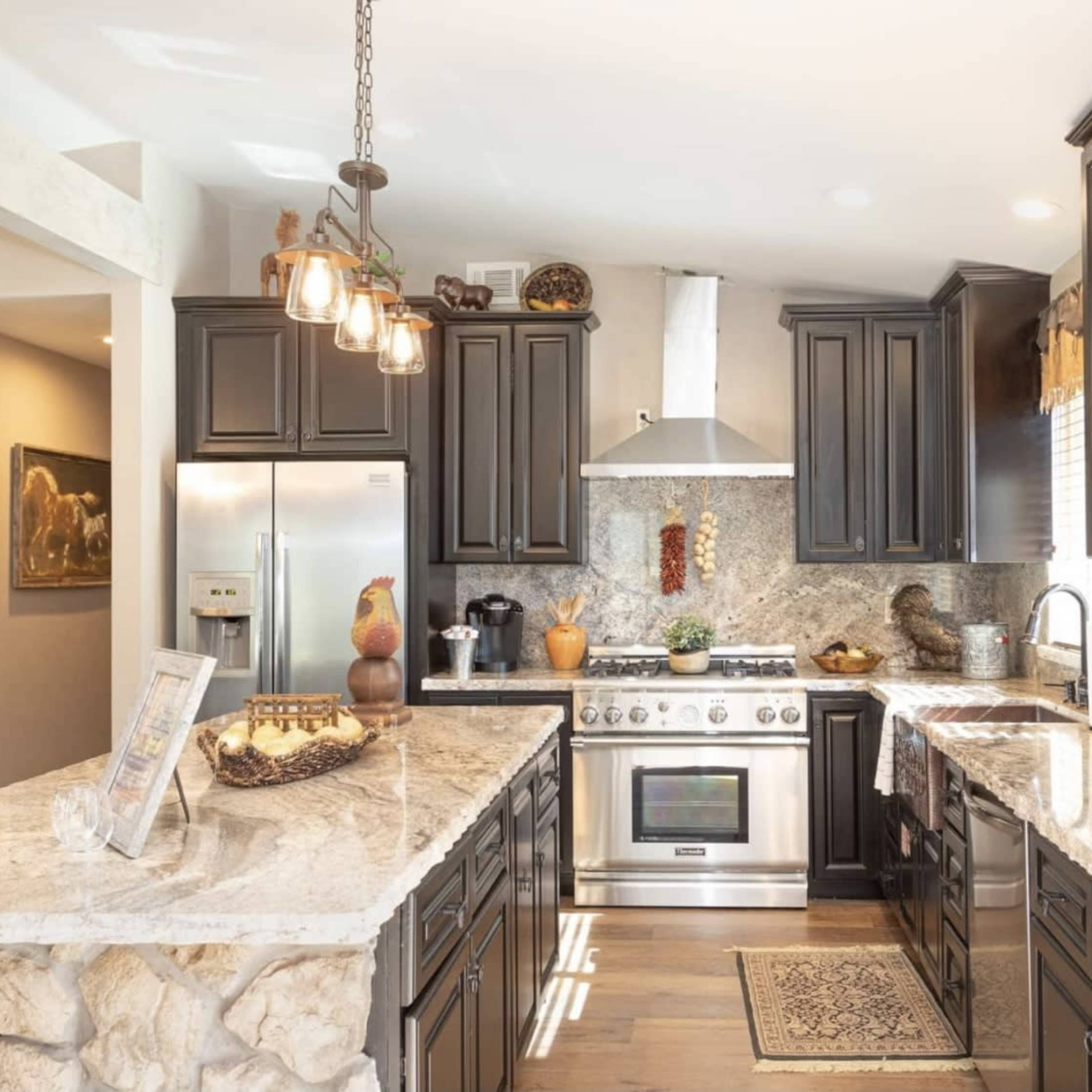 The kitchen features dark cabinetry, a marble counter, stainless steel appliances, and decorative elements throughout.
