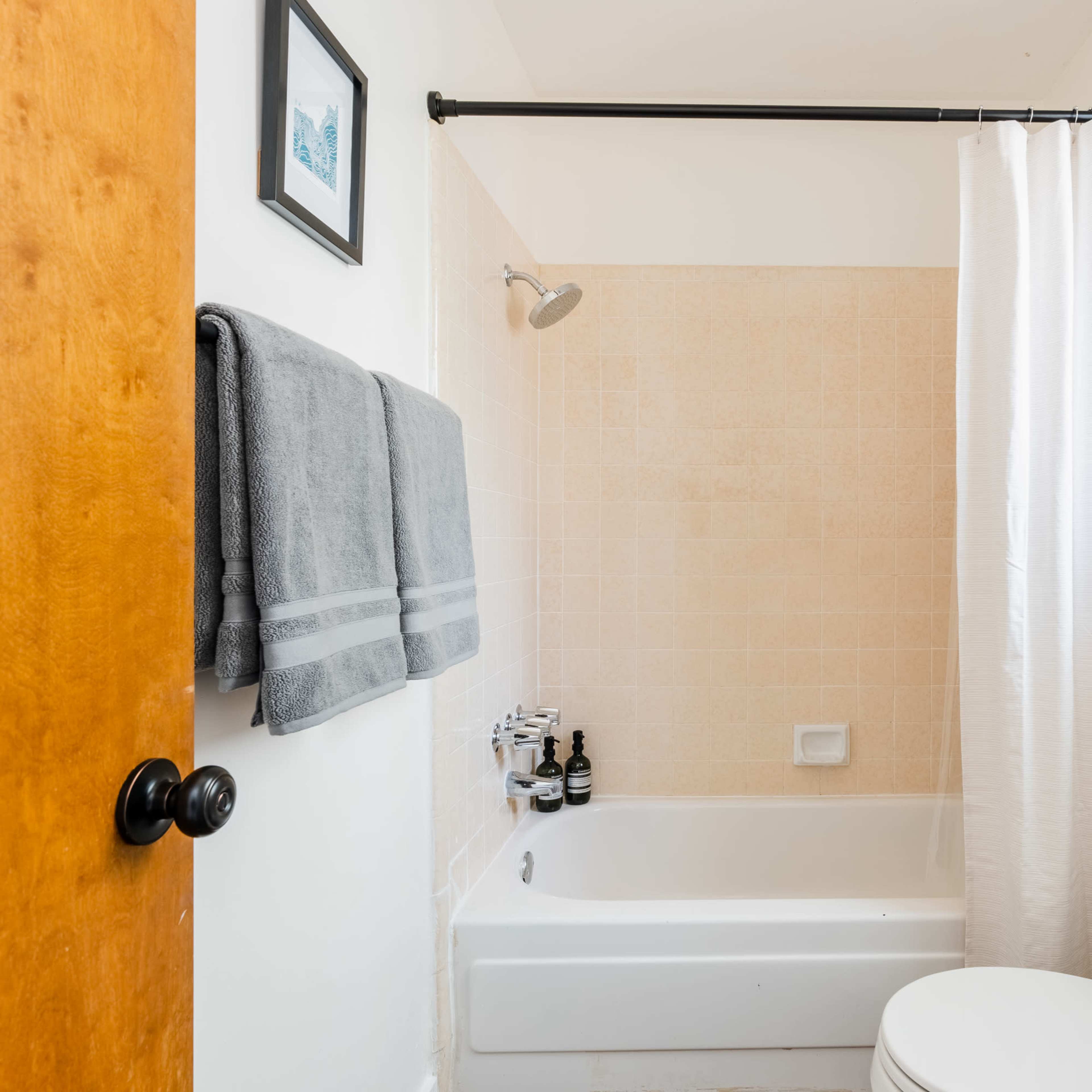 A bathroom featuring a bathtub with a shower, a toilet, a sink, and a window with a plant.