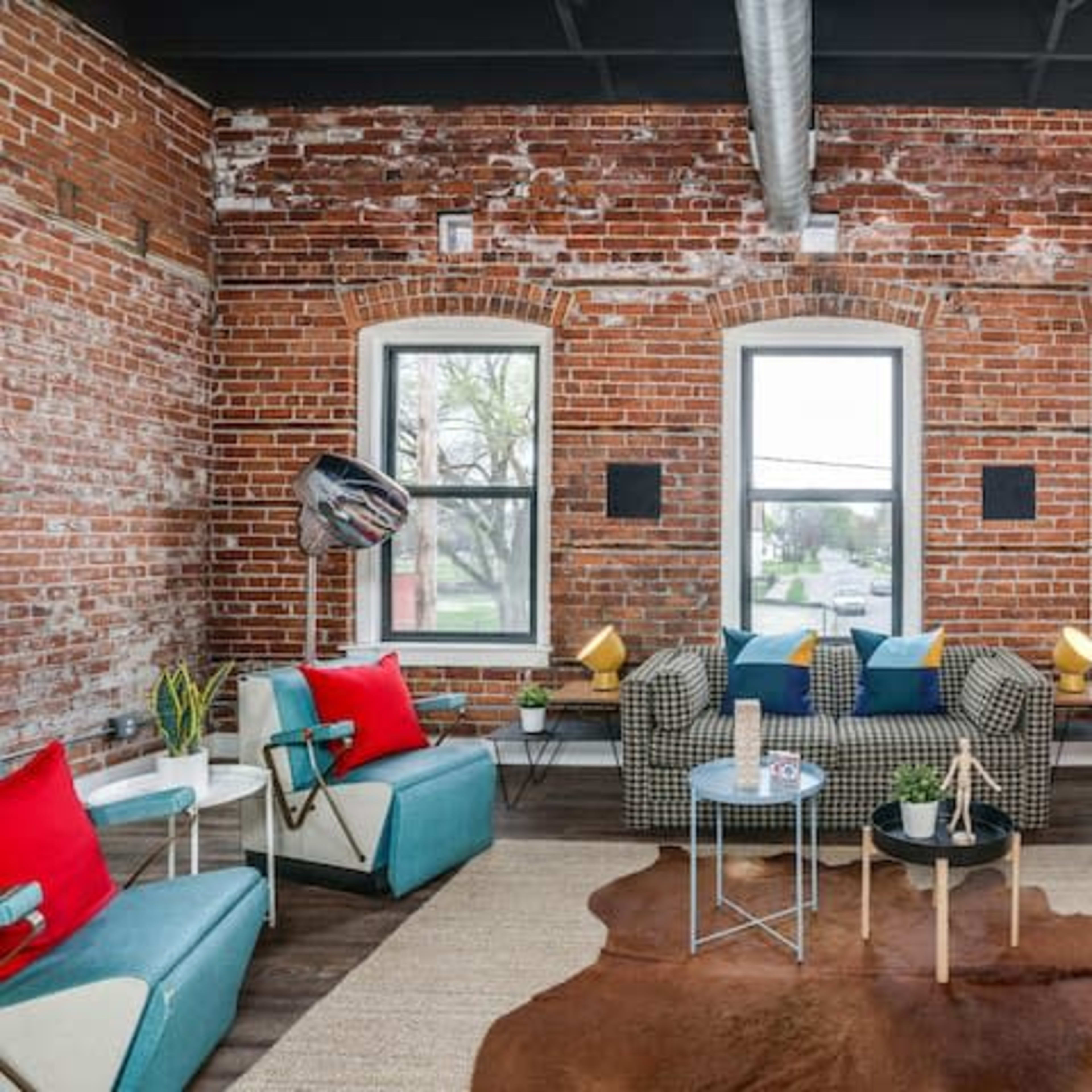 A stylish living room with exposed brick walls, large windows, and modern furniture arranged around a central coffee table.