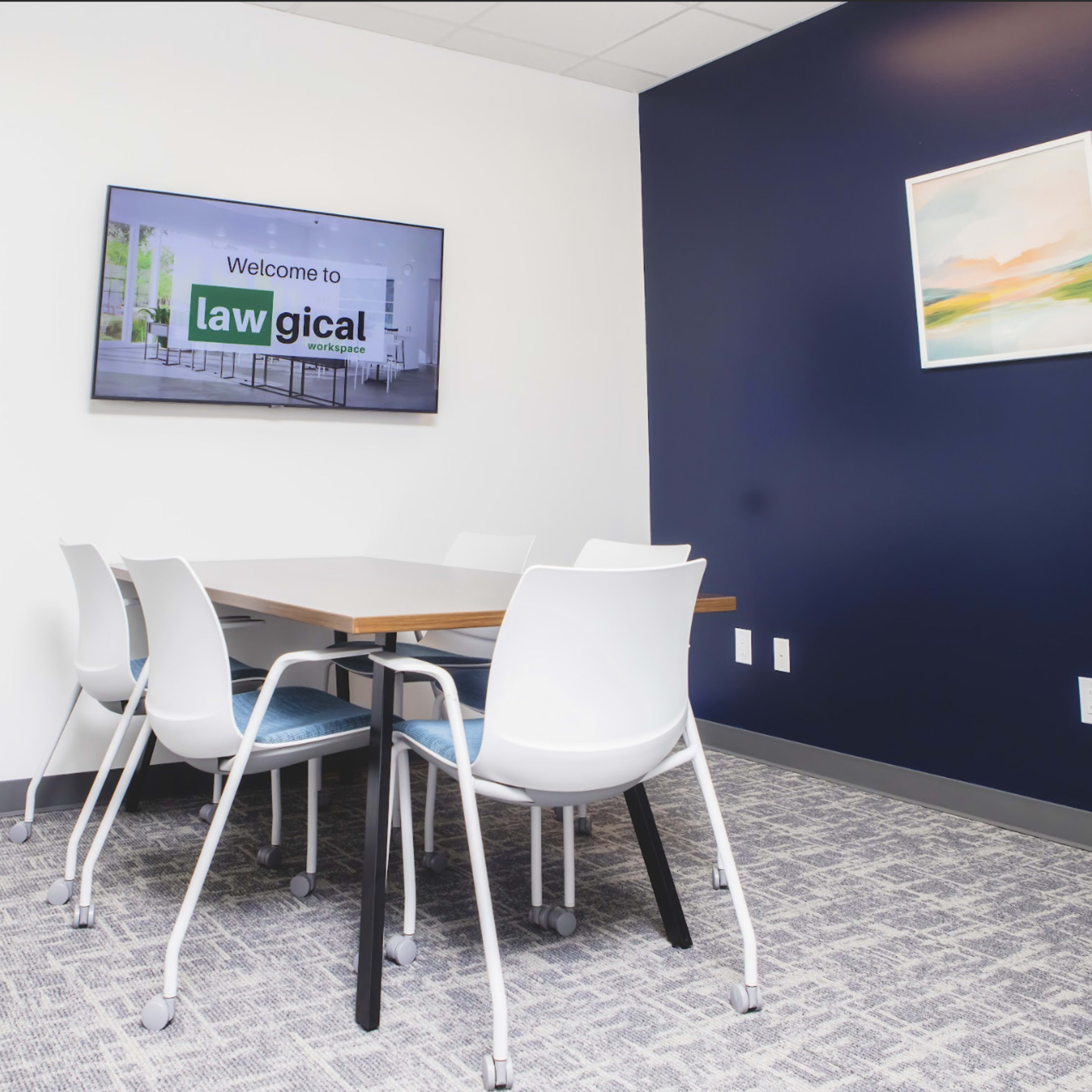 A conference room features a table surrounded by white chairs and a wall-mounted screen displaying "Welcome to law gical."