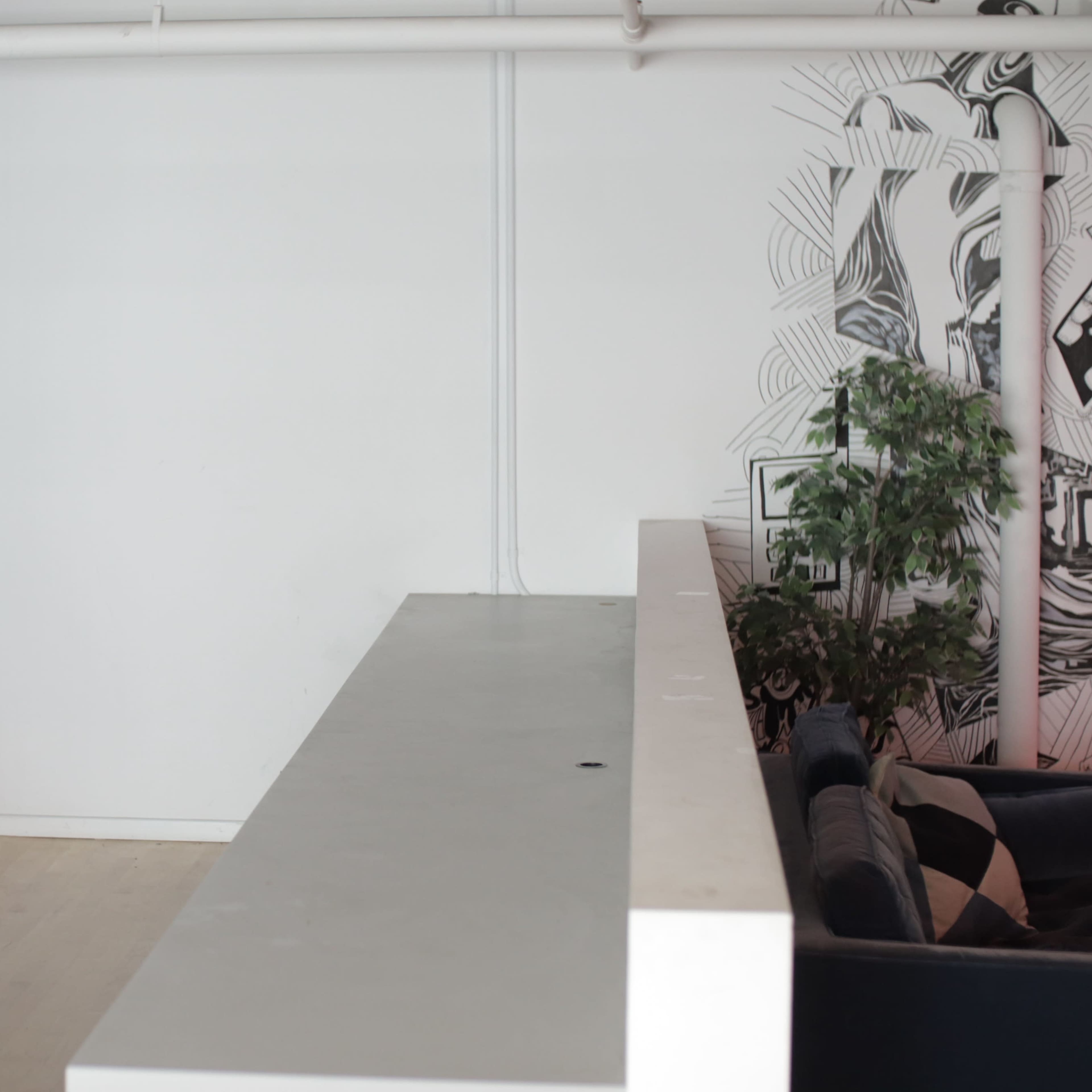 A minimalist interior space featuring a large concrete countertop against a white wall, with a window displaying green glass panels and plants nearby.
