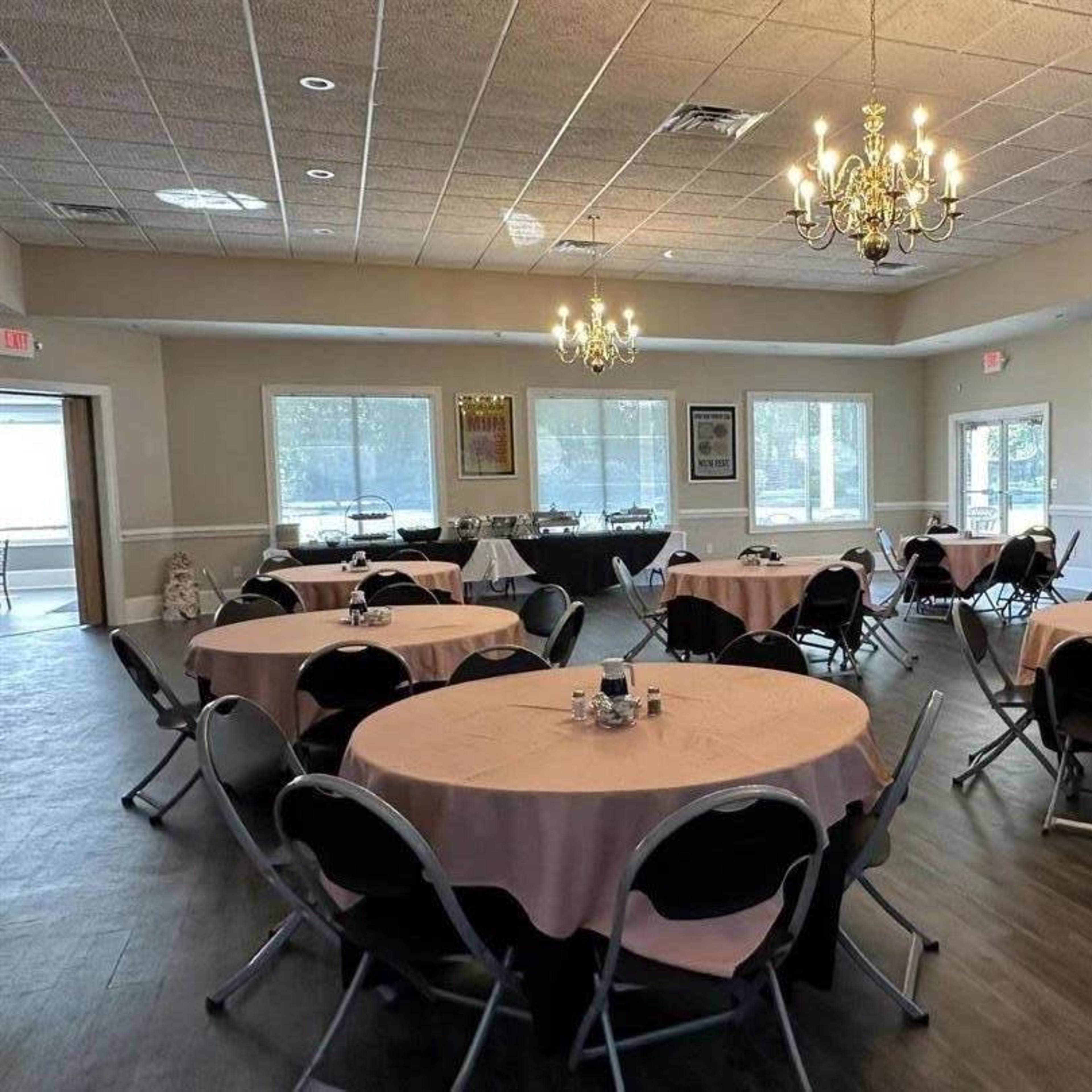 A spacious banquet room arranged with round tables covered in pink tablecloths and decorated with centerpieces, illuminated by chandeliers.