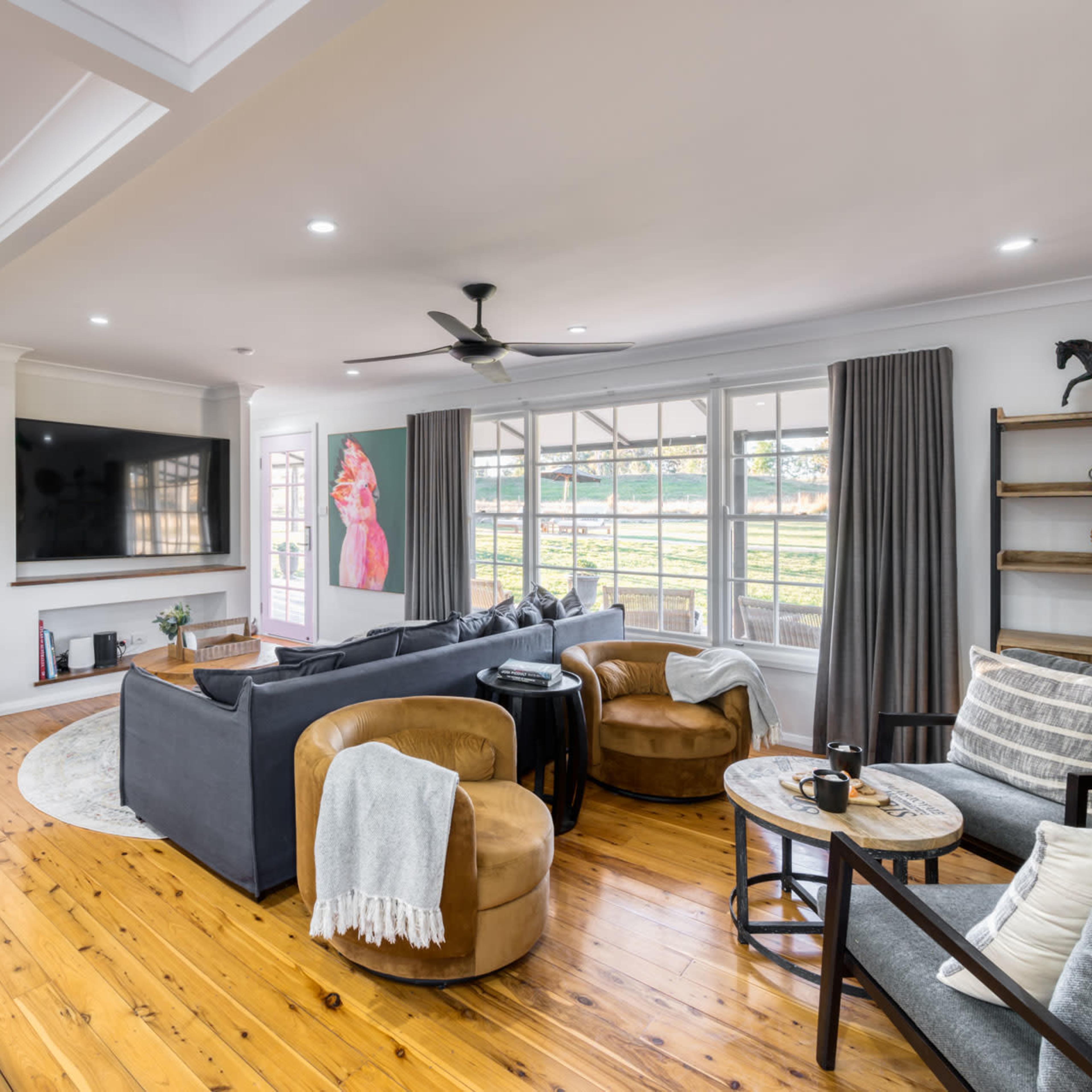 A modern living room with a gray sectional sofa, brown accent chairs, a wooden coffee table, and large windows allowing natural light.