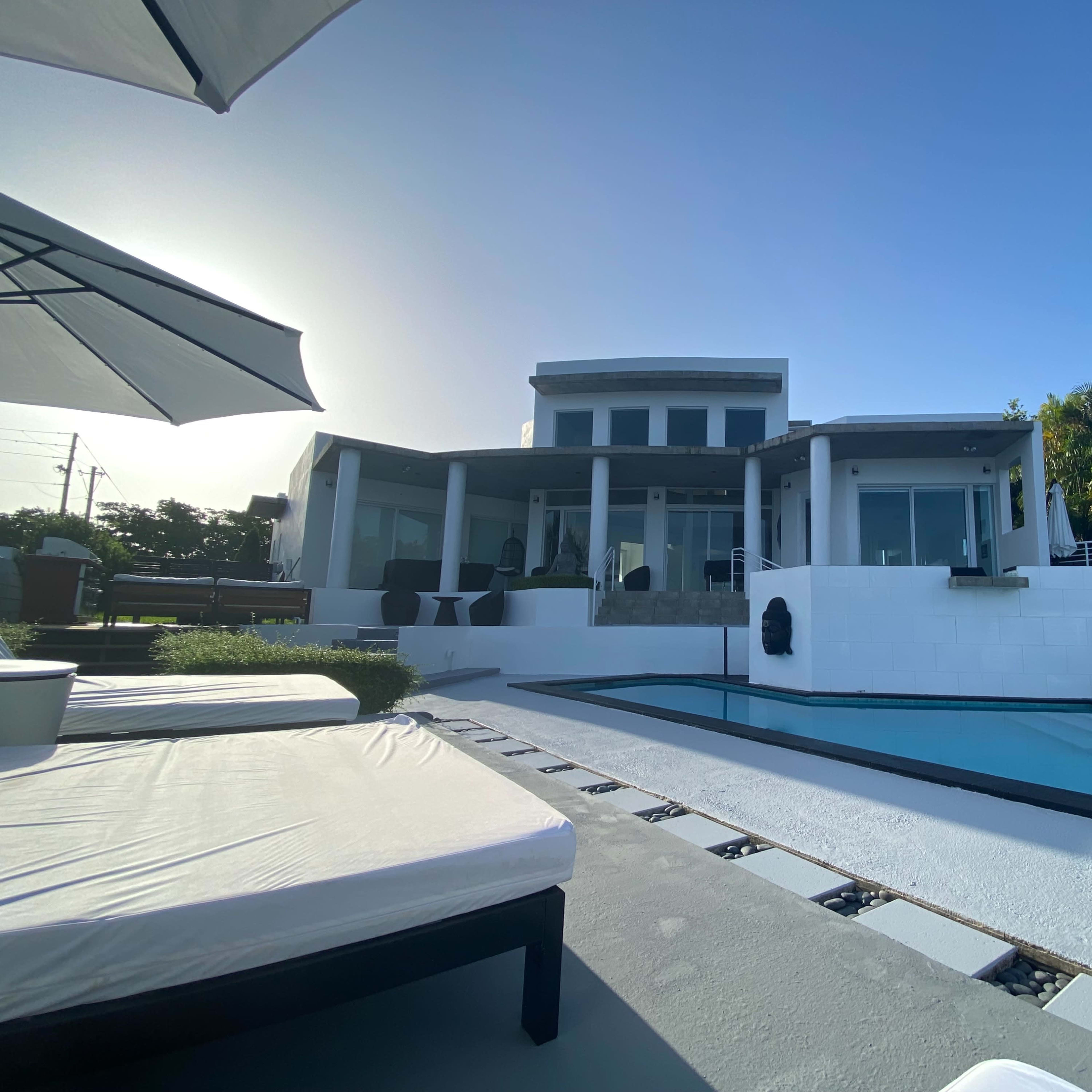 A modern house with large glass windows overlooks a swimming pool and a landscaped yard.