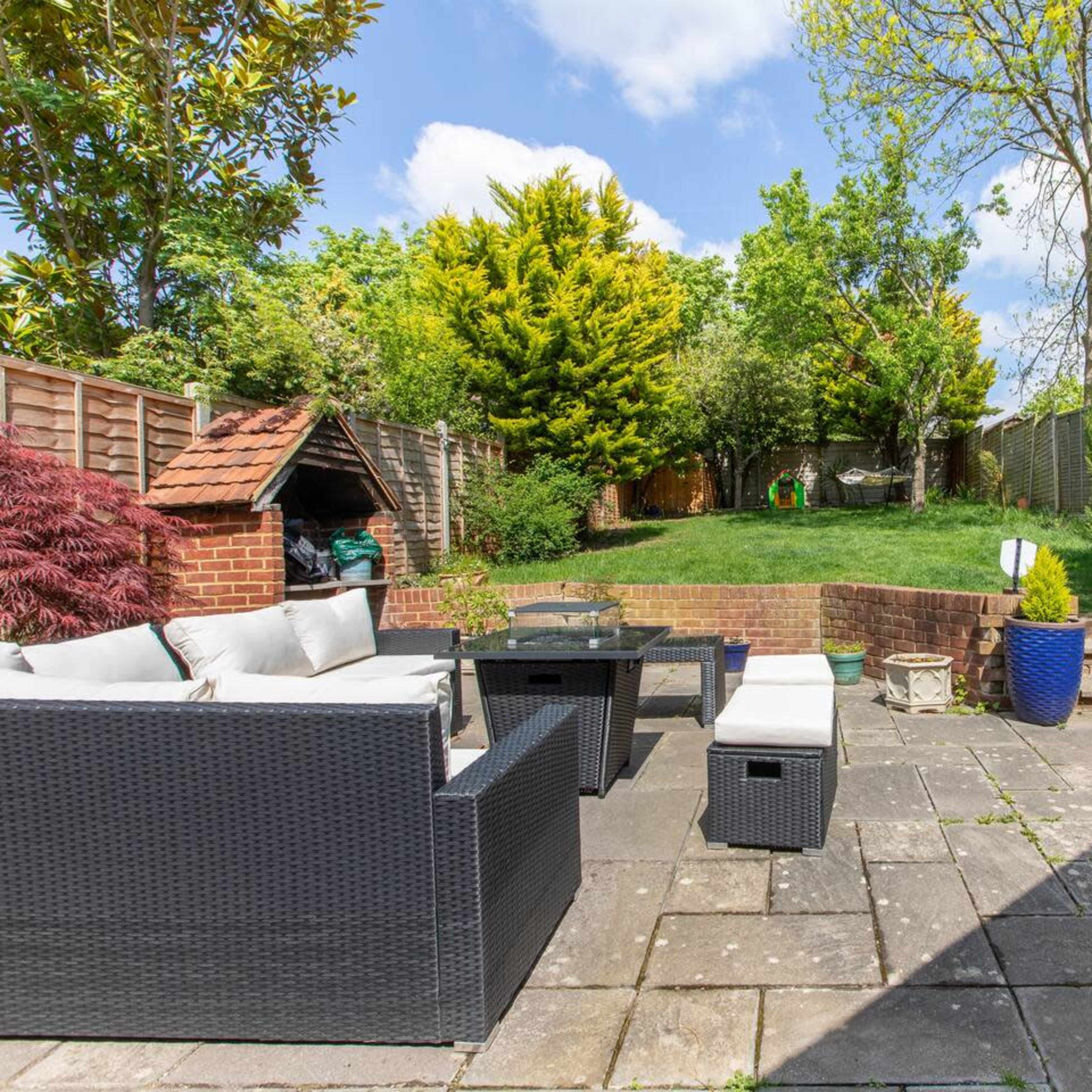 A patio area with outdoor furniture overlooks a grassy yard surrounded by trees and shrubs.