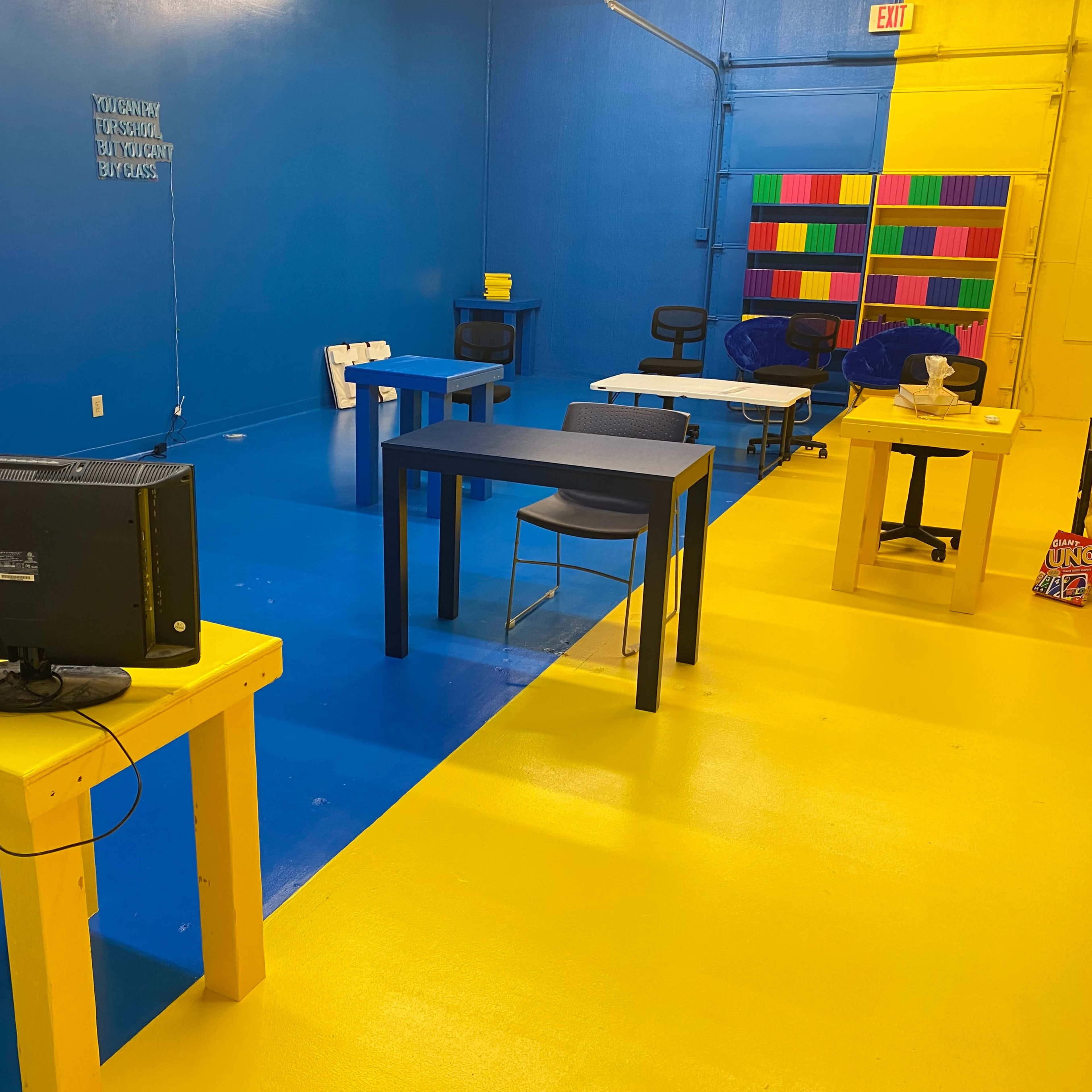 A brightly colored room with blue and yellow floors, featuring several tables and chairs, along with an old television set on a yellow table.