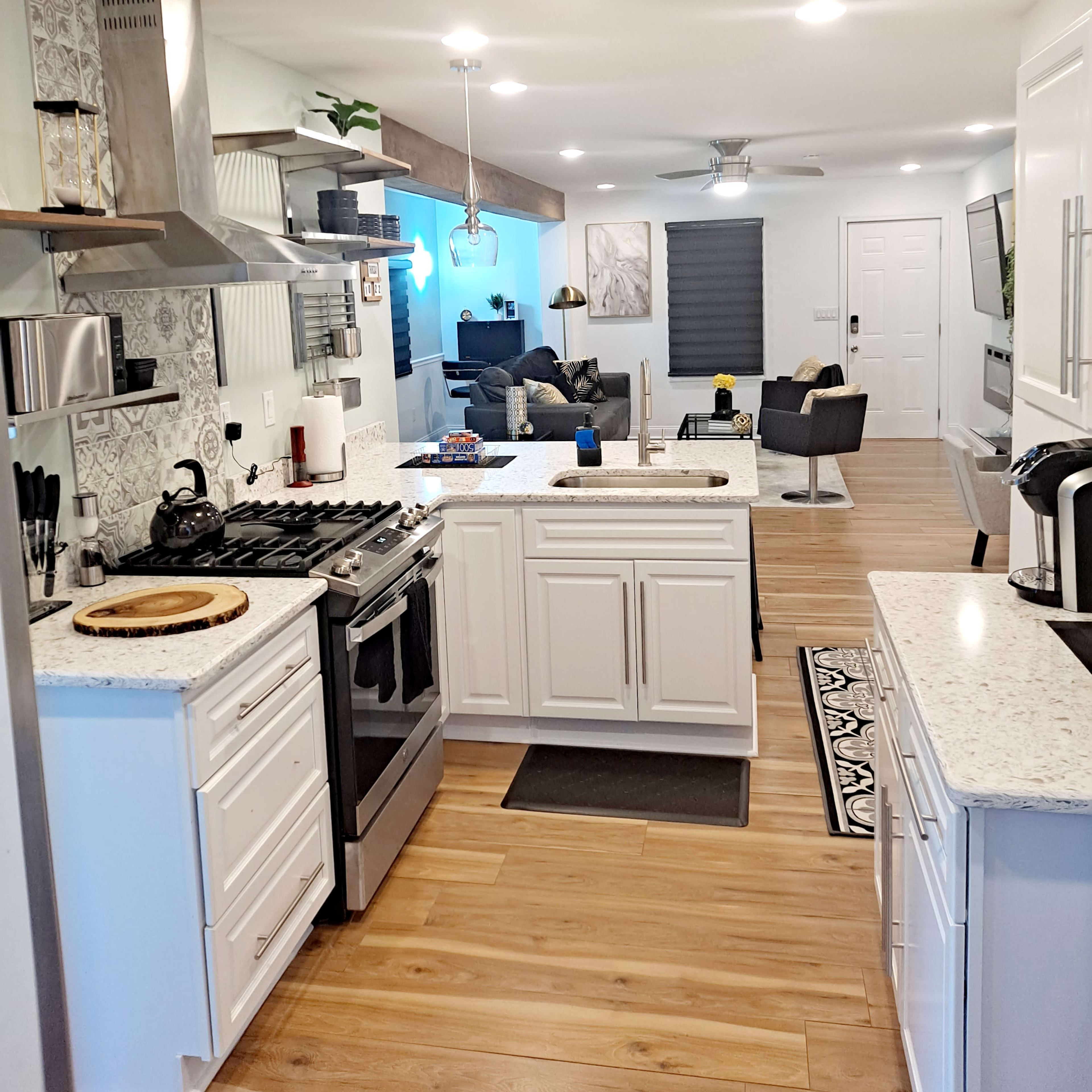 A modern kitchen with white cabinetry and a view into a living area featuring a sofa and flat-screen TV.