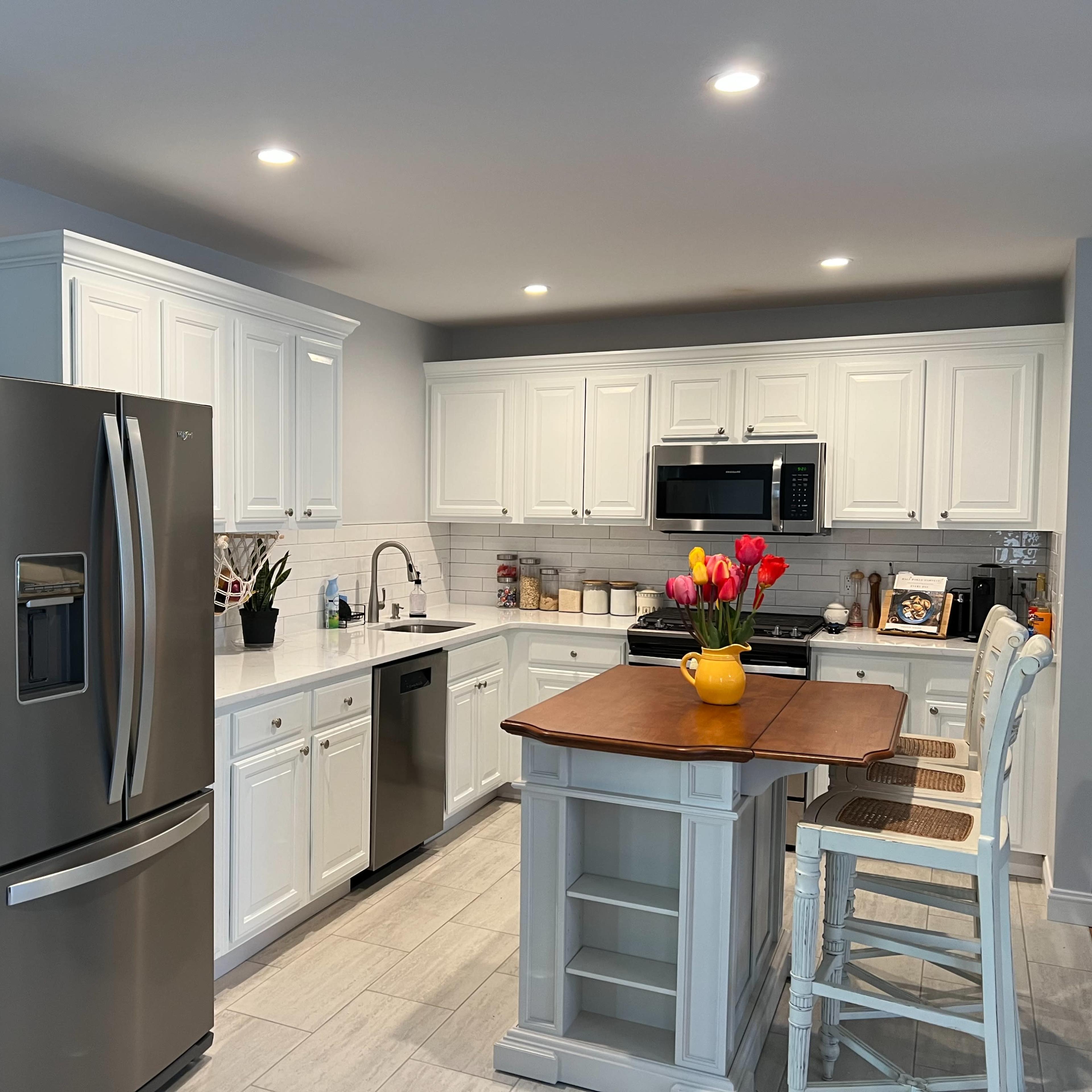 A modern kitchen with white cabinetry, stainless steel appliances, and a central island with a wooden top and seating.